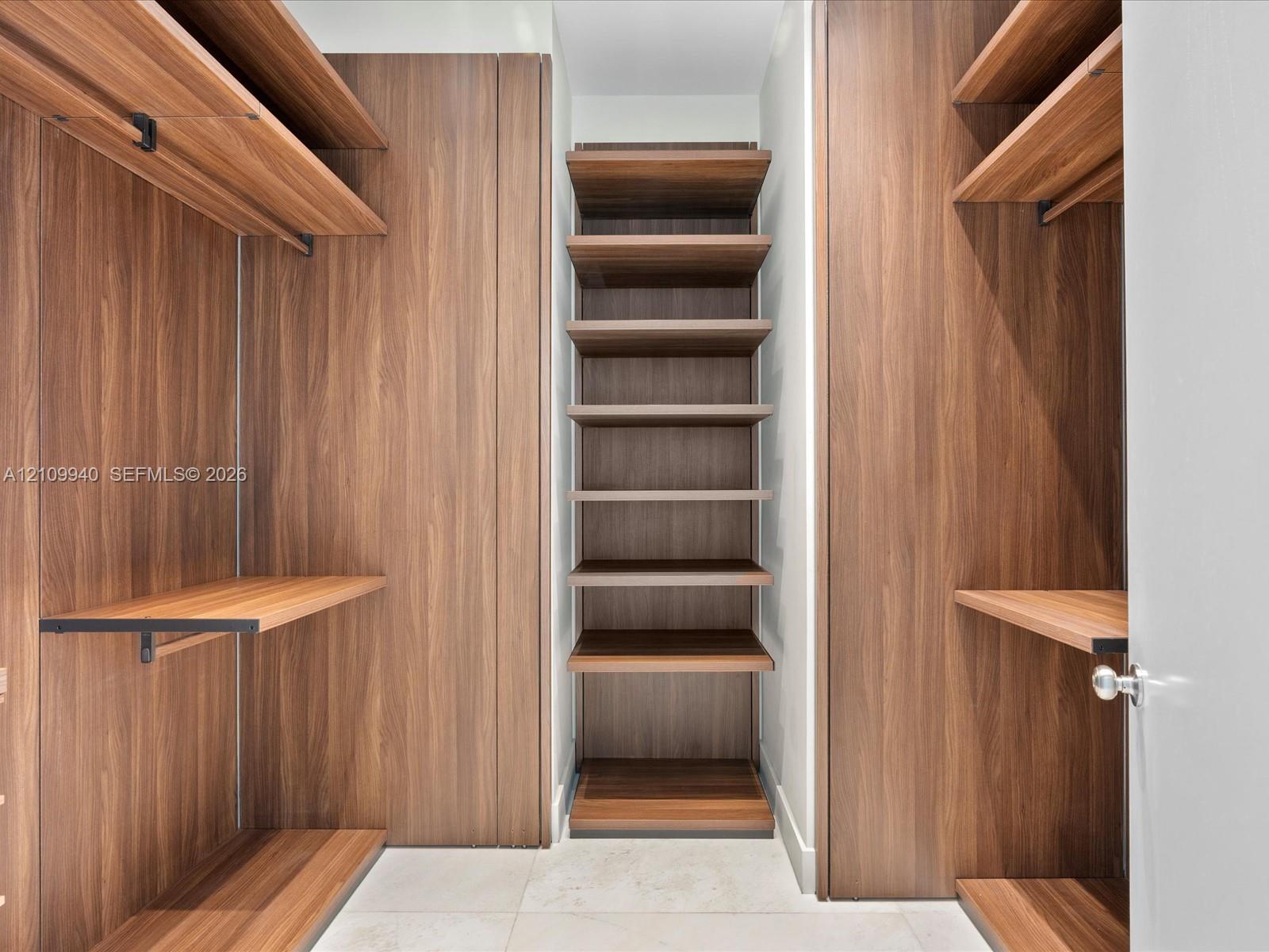 Walk-in closet featuring custom wood-finish cabinetry, built-in shelving units, hanging rods, and stone tile flooring