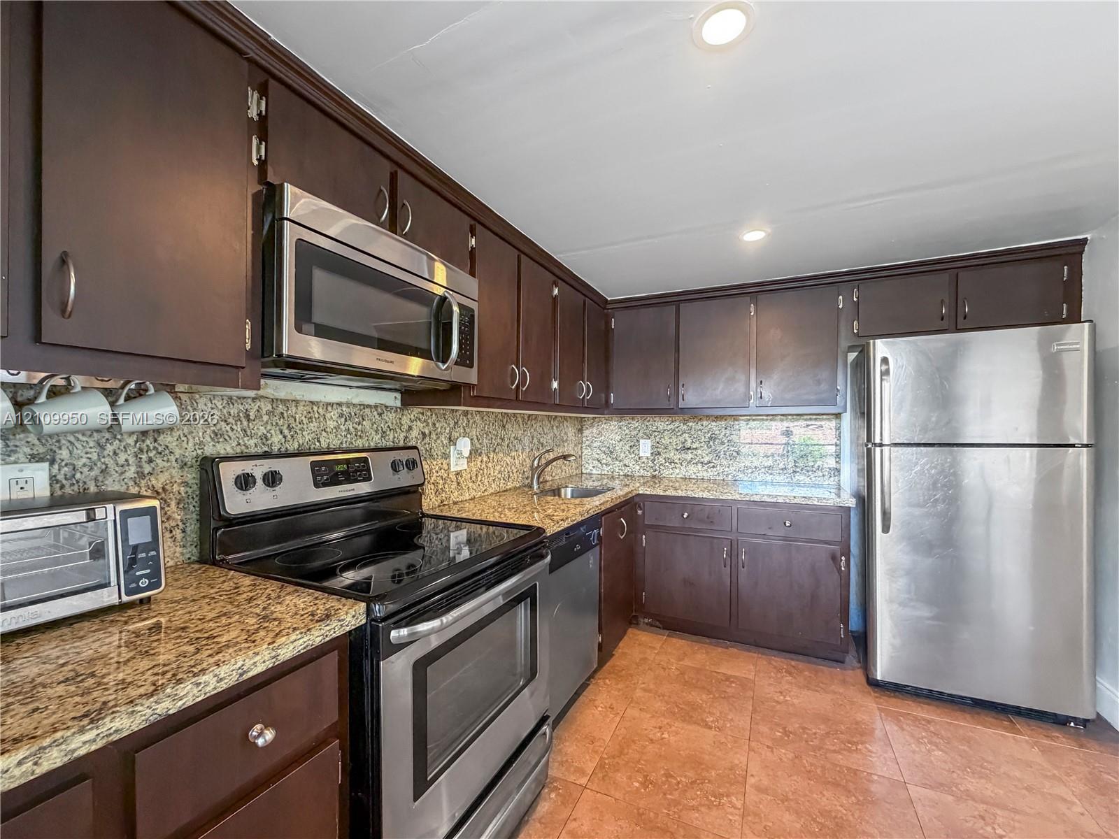 Kitchen featuring dark wood cabinetry, stainless steel appliances, stone-patterned countertops, and tile flooring
