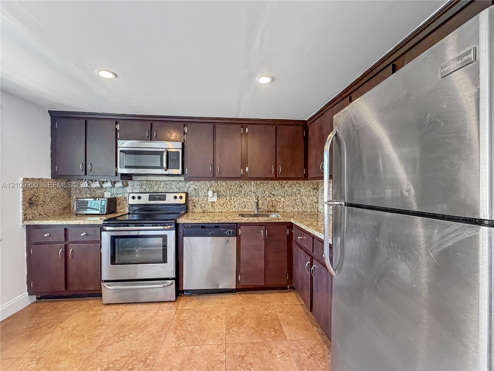 Kitchen featuring dark wood cabinetry, stone-finish countertops, tile flooring, and integrated stainless steel appliances