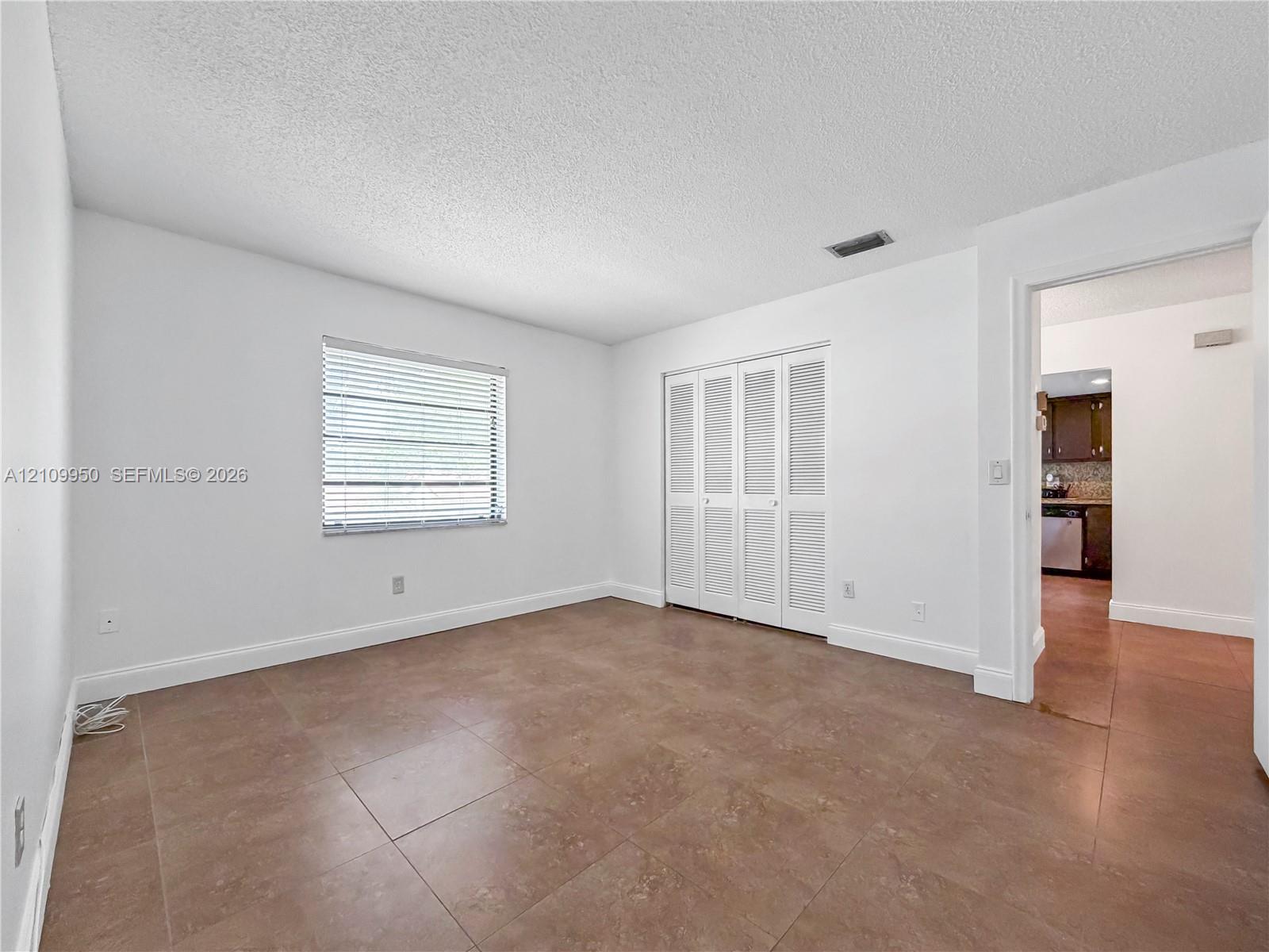 Neutral interior space featuring large-format ceramic tile flooring, a window with horizontal blinds, and a built-in four-panel folding closet door