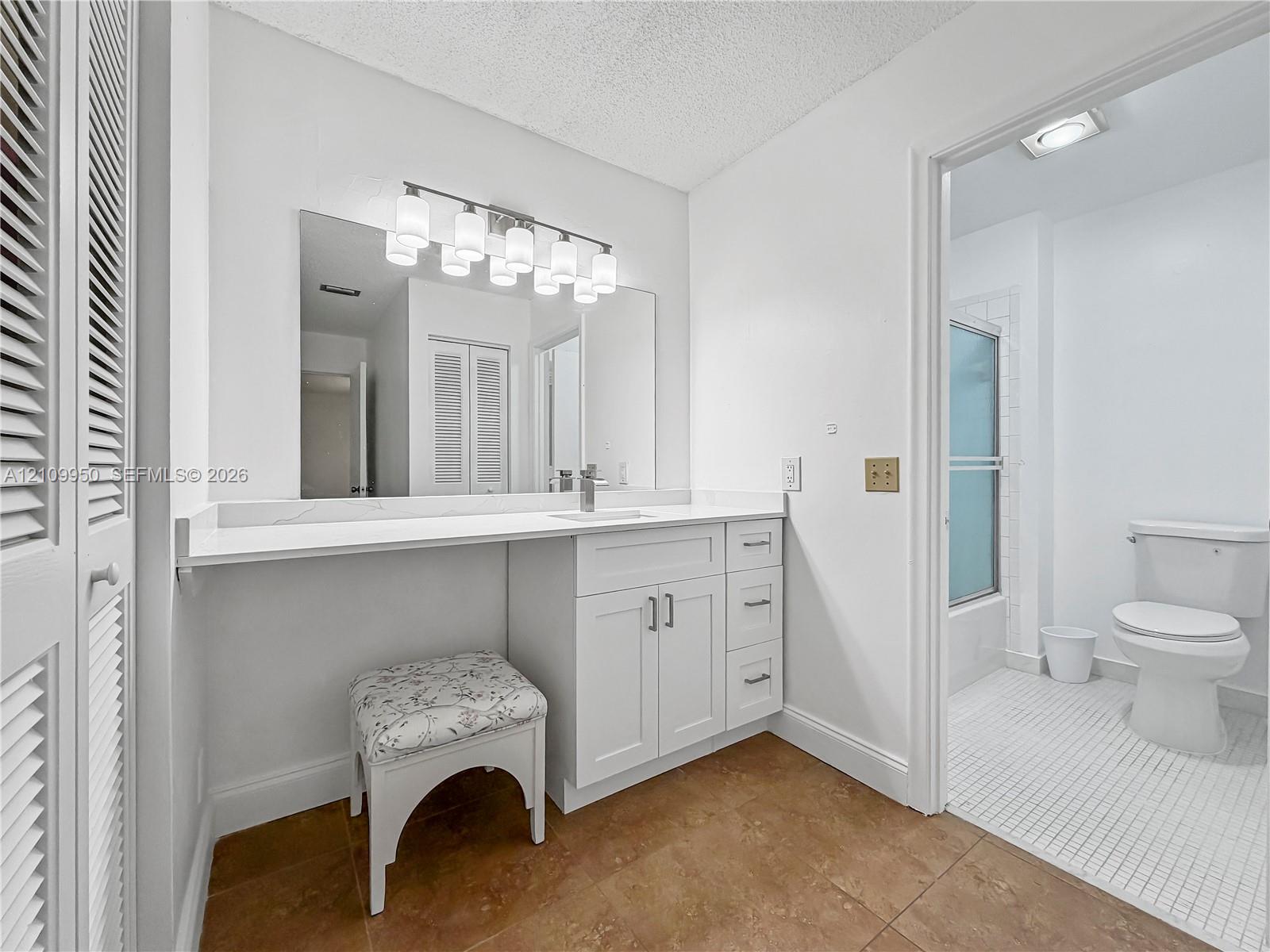 Bathroom featuring a white vanity with extended countertop, large wall-mounted mirror, multi-bulb lighting fixture, and a tile floor