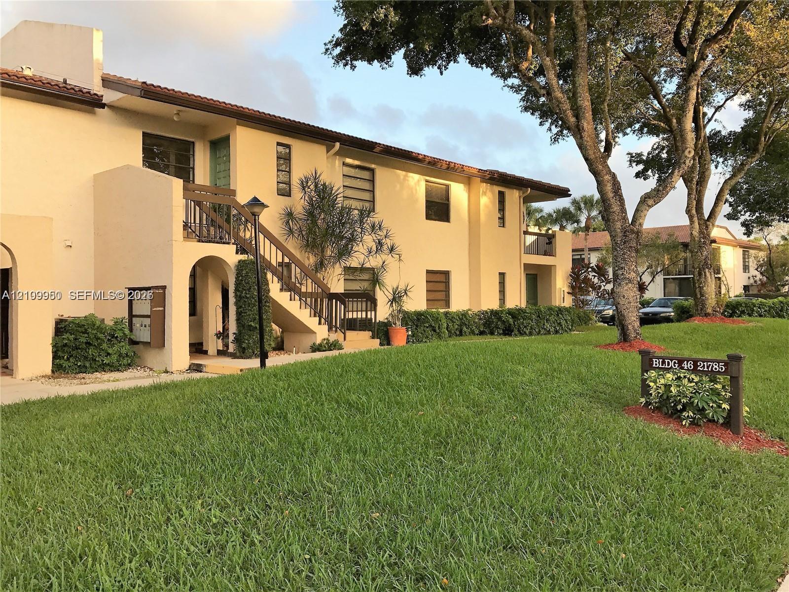 Stucco exterior featuring multi-level open-air staircases, integrated wooden railings, tile roofing, and mature shade trees