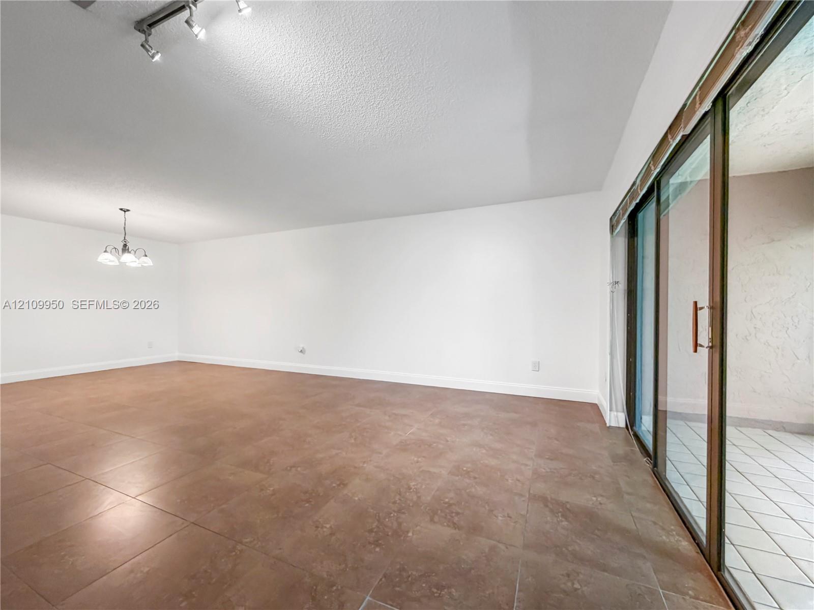 Open-concept interior featuring large-format stone-finish tile flooring, ceiling-mounted track lighting, a multi-arm chandelier, and sliding glass doors