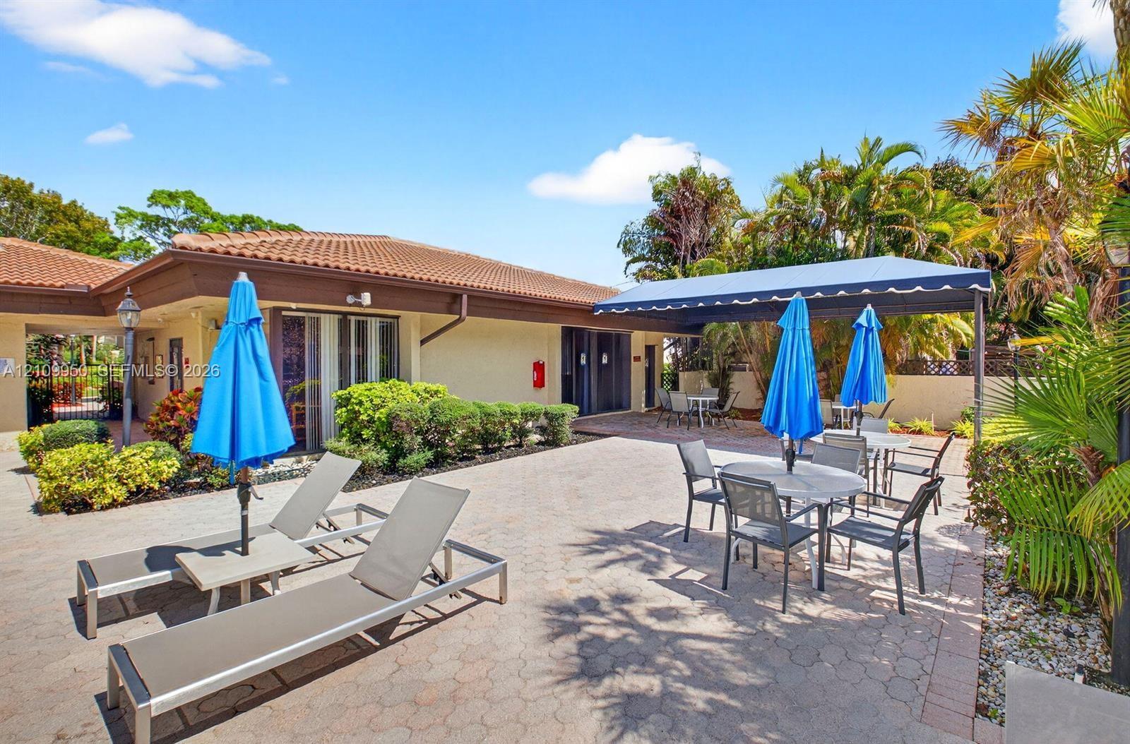 Paver patio featuring a fixed fabric awning, stucco exterior, clay tile roofing, and integrated mature landscaping