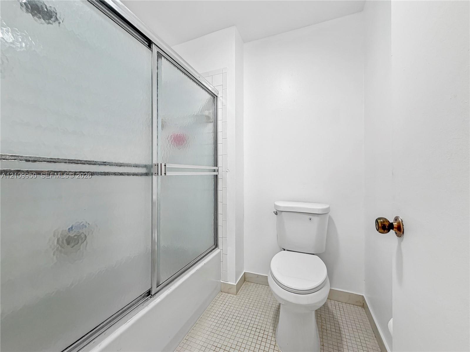 Bathroom featuring a shower with a sliding metal-framed textured glass enclosure, white tile shower surround, and square floor tiling