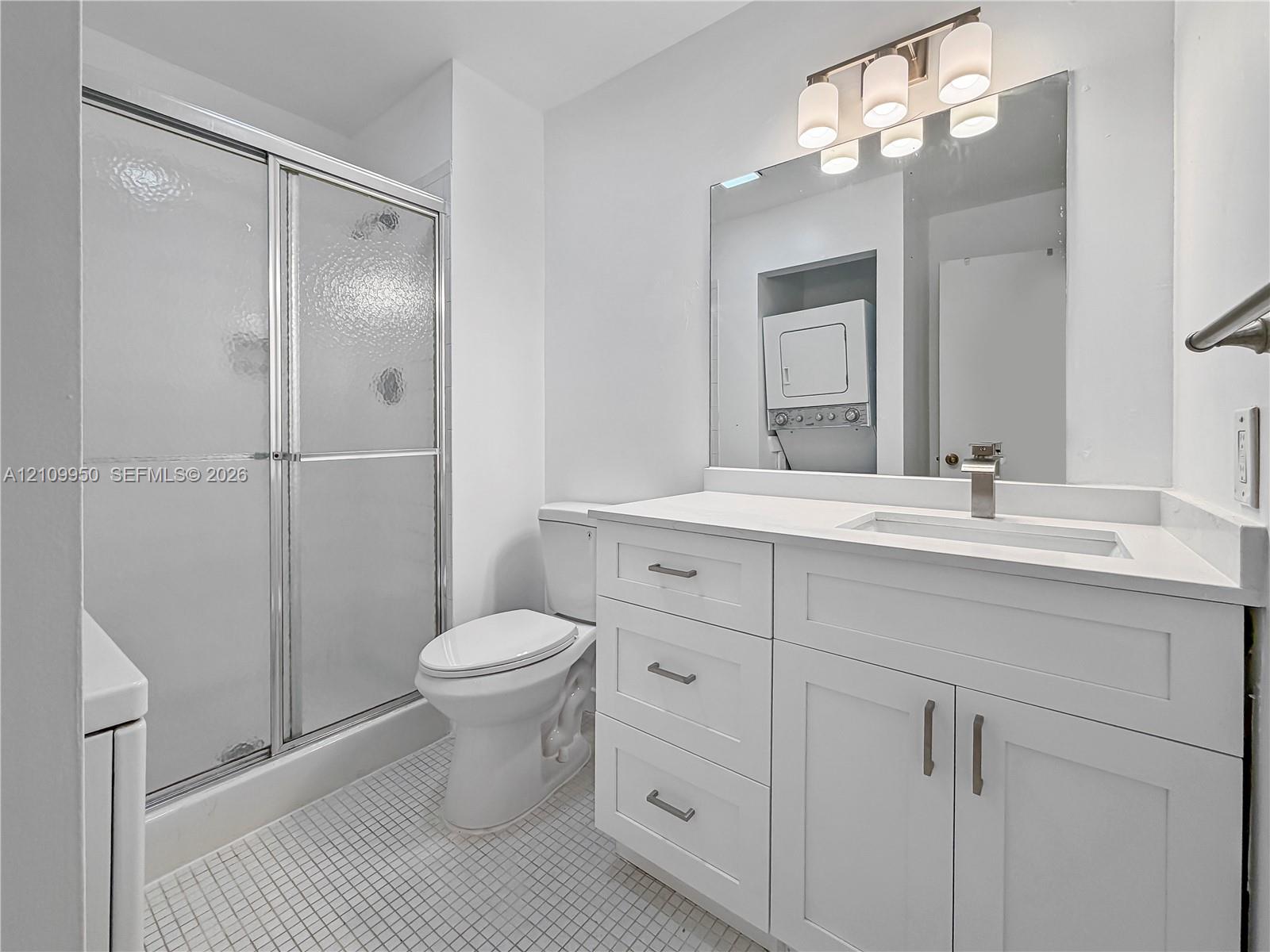 Bathroom featuring a white vanity with a rectangular sink, brushed metal faucet, shower with glass sliding doors, and four-light vanity fixture