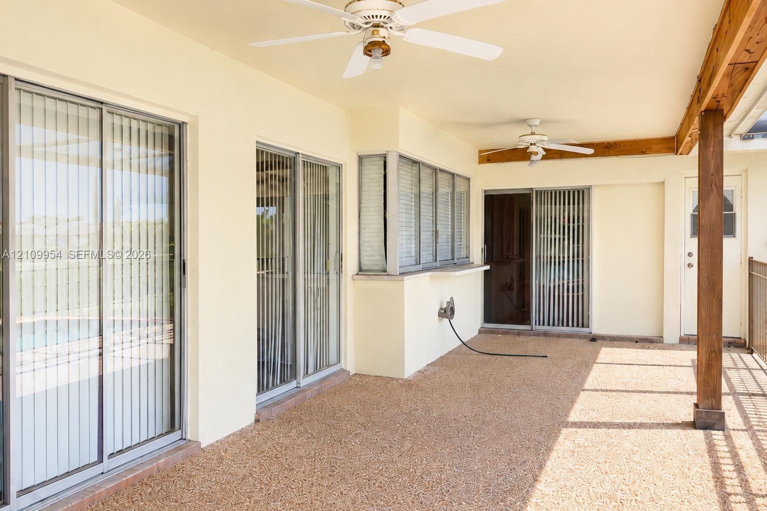 Covered patio featuring aggregate concrete flooring, dual ceiling fans, multiple sliding glass door entries, and exposed timber support beams