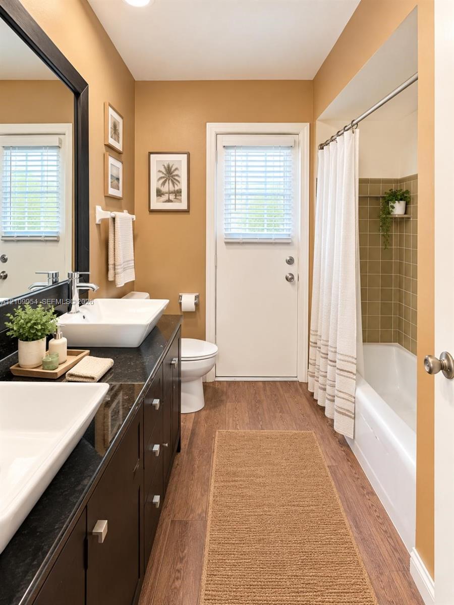 Dark-finish vanity with dual rectangular vessel sinks, contrasting solid-surface countertop, wood-finish flooring, and a tub-shower combination with tiled surround Dark-finish vanity with dual rectangular vessel sinks, contrasting solid-surface countertop, wood-finish flooring, and a tub-shower combination with tiled surround