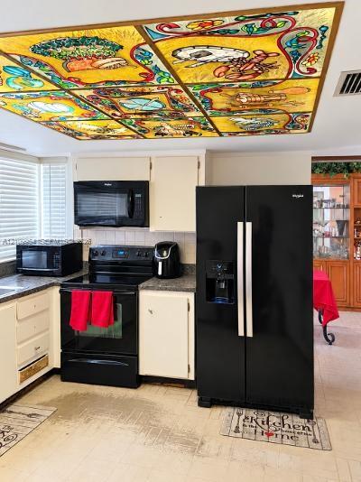 Custom multi-panel stained glass ceiling feature, black finish side-by-side refrigerator, matching black range with integrated microwave, and white cabinetry Custom multi-panel stained glass ceiling feature, black finish side-by-side refrigerator, matching black range with integrated microwave, and white cabinetry