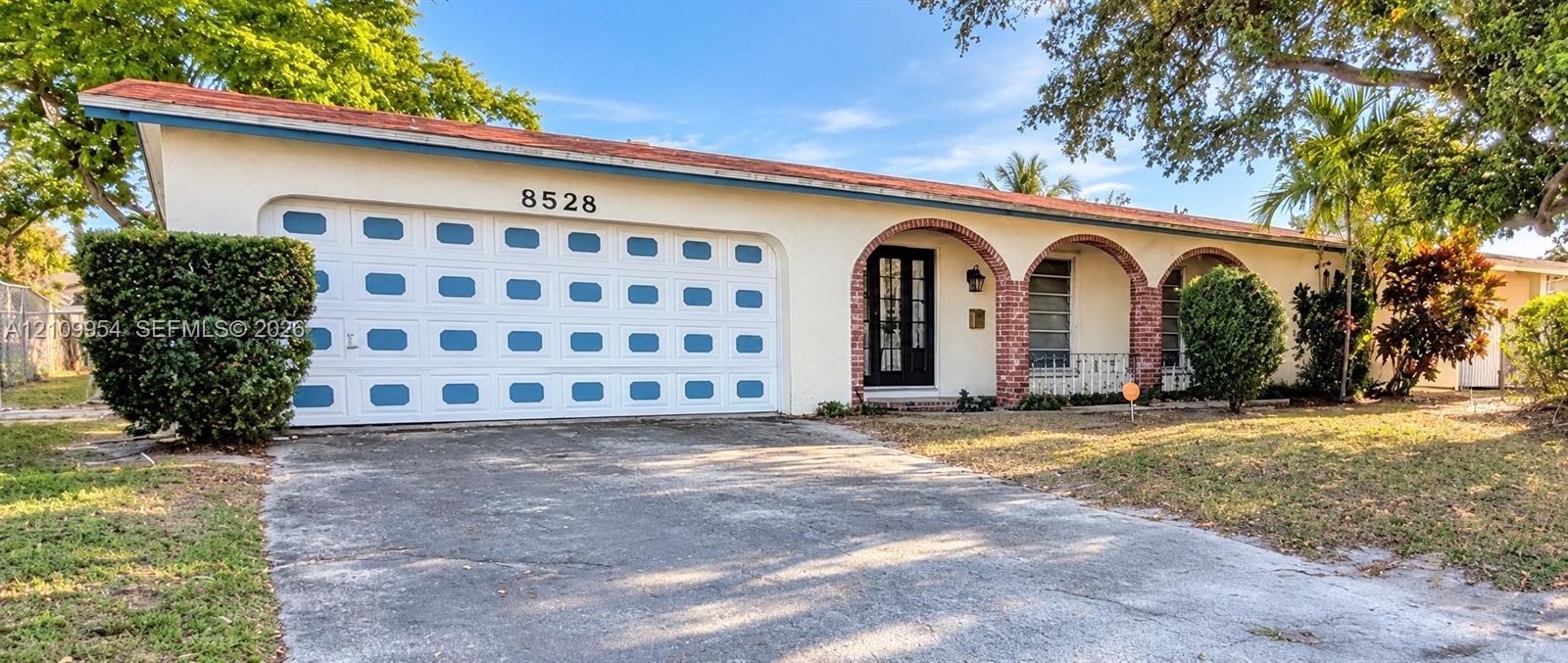Single-story residence featuring a terracotta-tiled roof, white exterior, arched masonry entryway, multi-panel garage door, and metal window grilles Single-story residence featuring a terracotta-tiled roof, white exterior, arched masonry entryway, multi-panel garage door, and metal window grilles