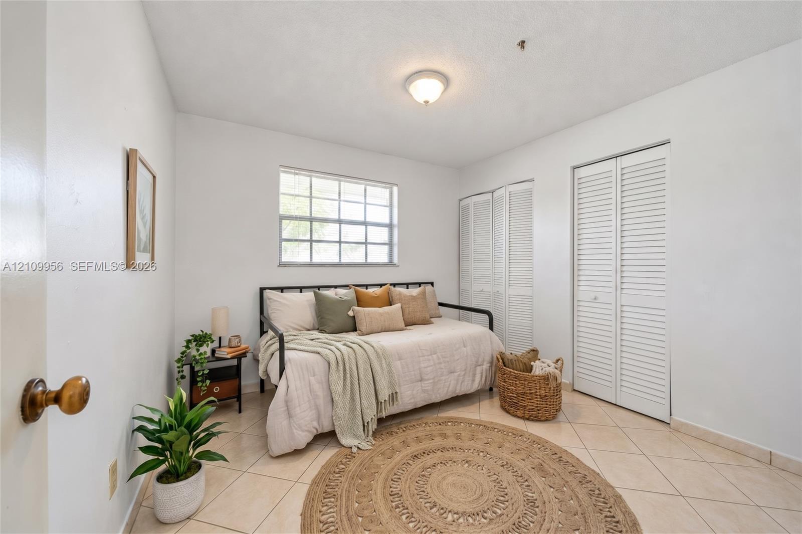 Interior space featuring neutral wall tones, ceramic tile flooring, a multi-pane window, and dual closets with louvered doors