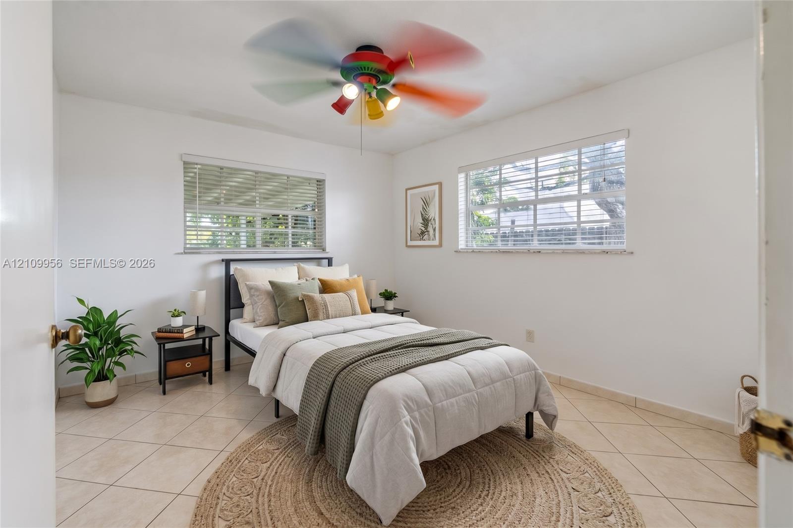 Neutral-toned ceramic tile flooring, dual windows with integrated horizontal blinds, and a multi-light ceiling fan