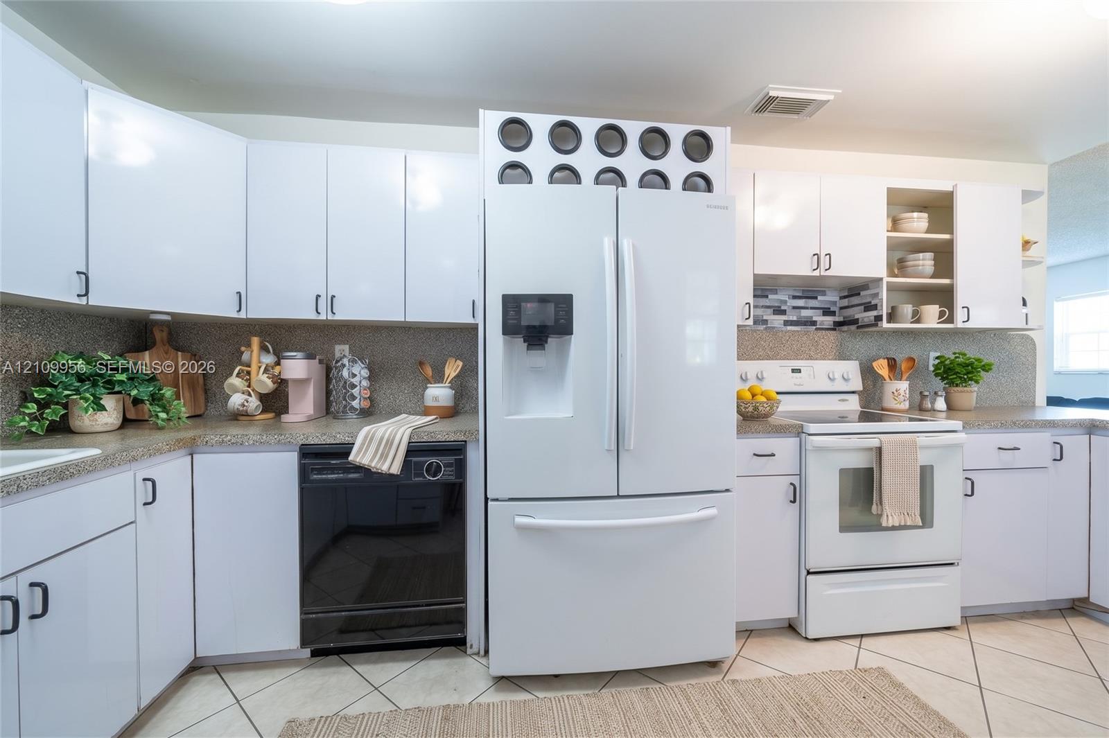 Kitchen featuring white shaker-style cabinetry, neutral stone-finish countertops, tiled backsplash, tile flooring, and integrated white appliances
