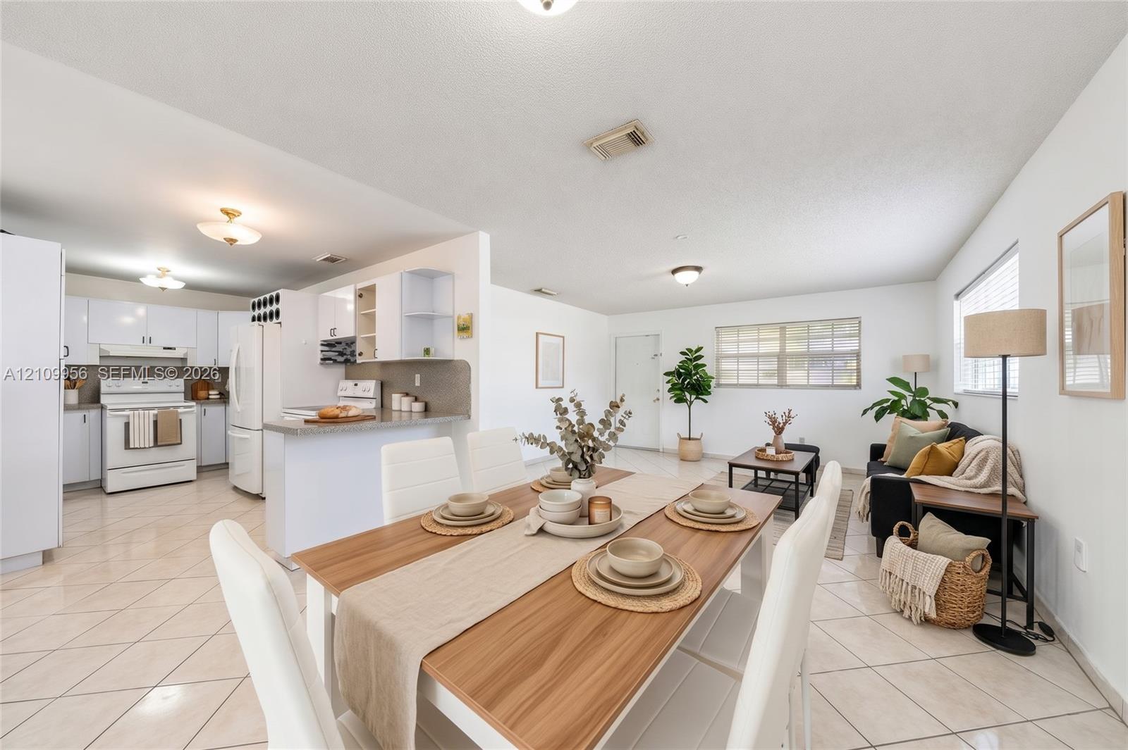 Open-concept interior featuring light-colored tile flooring, white cabinetry, integrated peninsula breakfast bar, and multiple flush-mount light fixtures