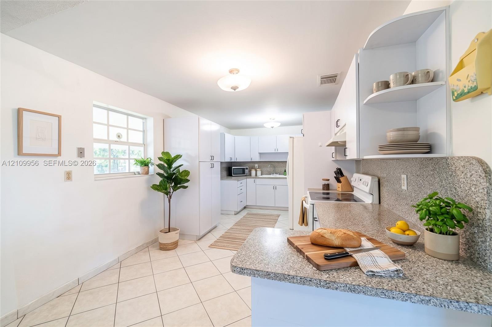 Kitchen featuring white cabinetry, solid surface countertops, a grid-pattern window, and neutral tile flooring