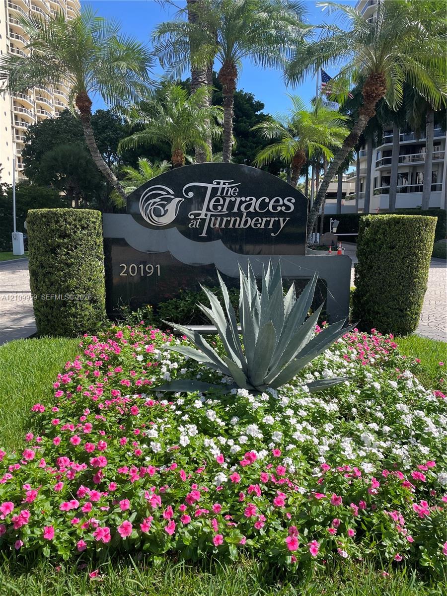 Monument sign for The Terraces at Turnberry featuring polished stone lettering, mature palm trees, sculpted hedges, and landscaped flower beds