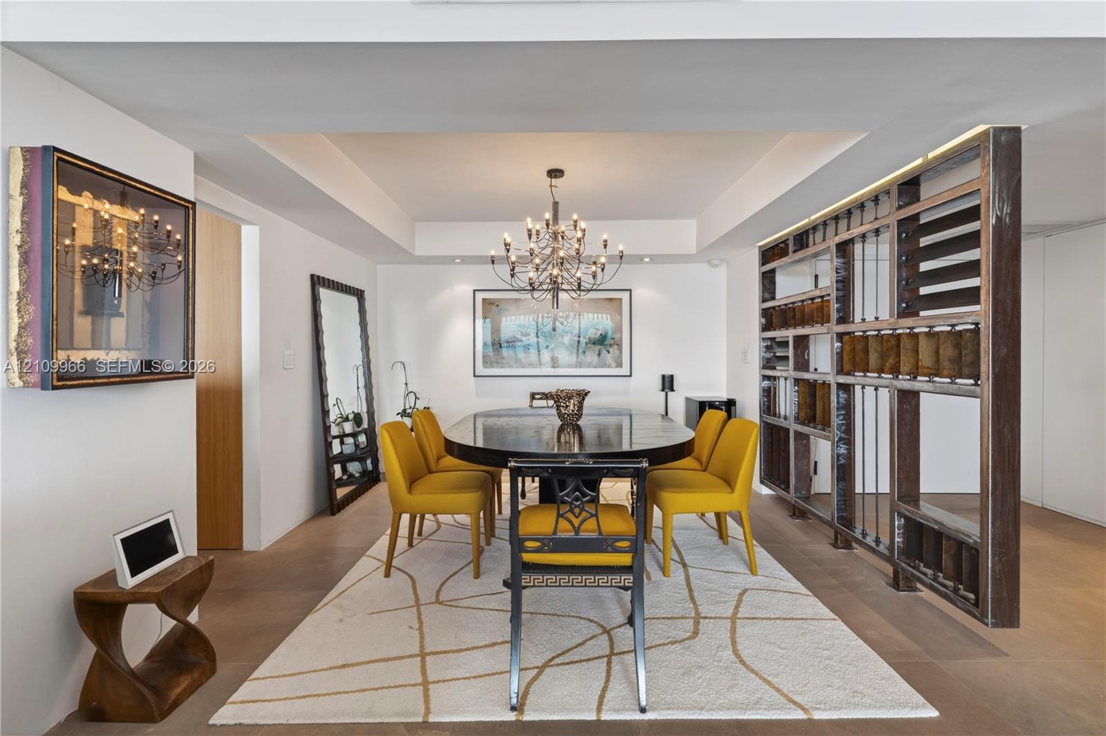 Tray ceiling with recessed lighting, custom floor-to-ceiling metal and glass open-frame partition, multi-arm chandelier, and wide-plank wood-finish flooring