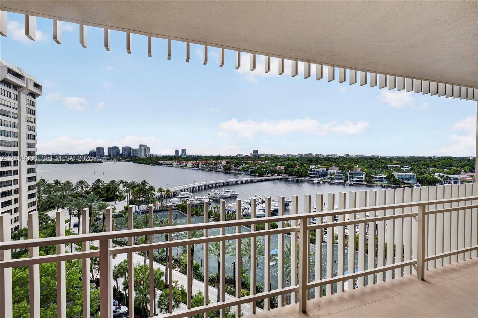 Covered balcony featuring vertical privacy screening and metal railing, overlooking a marina and waterfront landscape