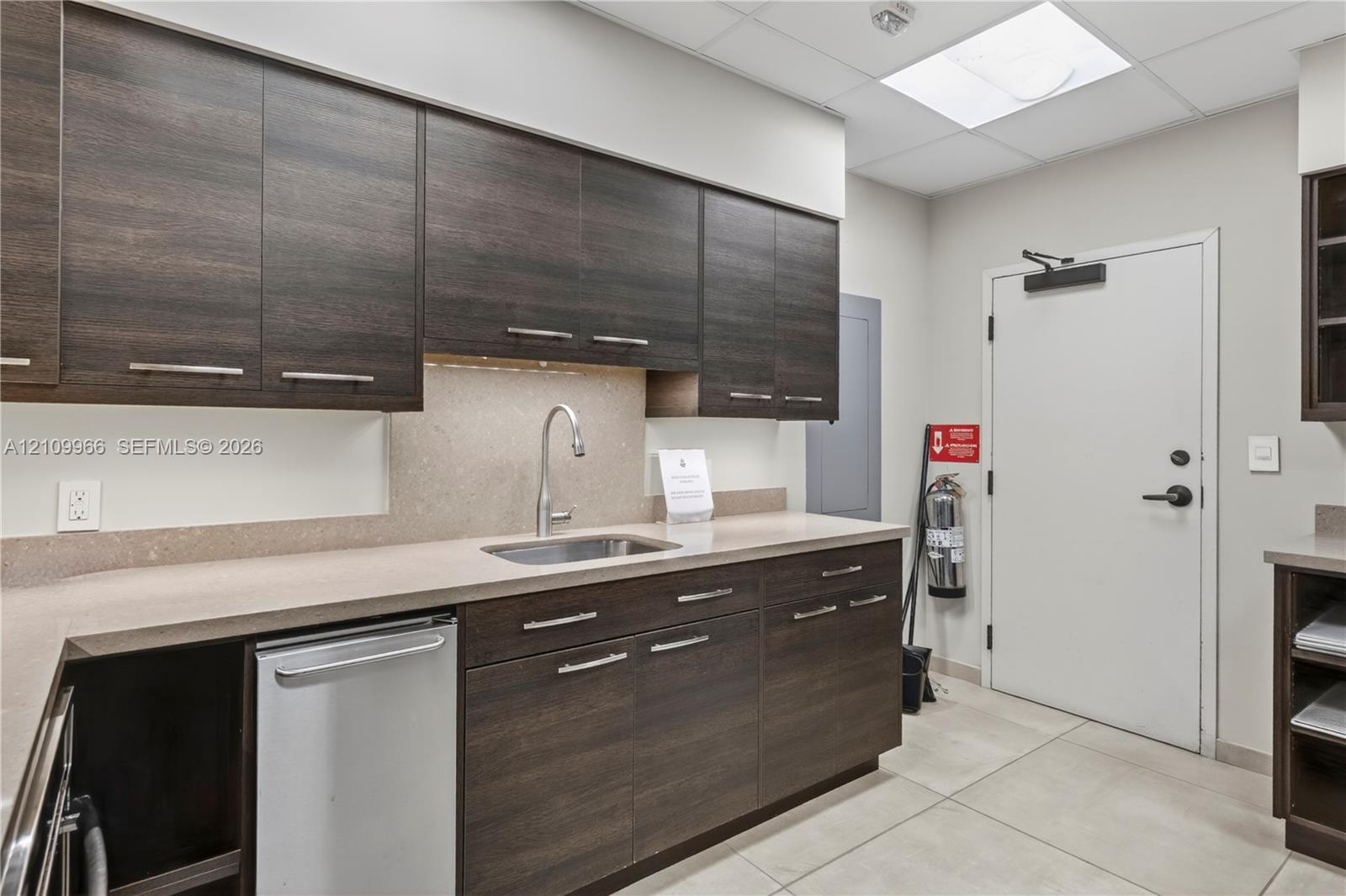 Kitchen area featuring dark wood-finish cabinetry, solid surface countertops, stainless steel undermount sink with gooseneck faucet, and tile flooring