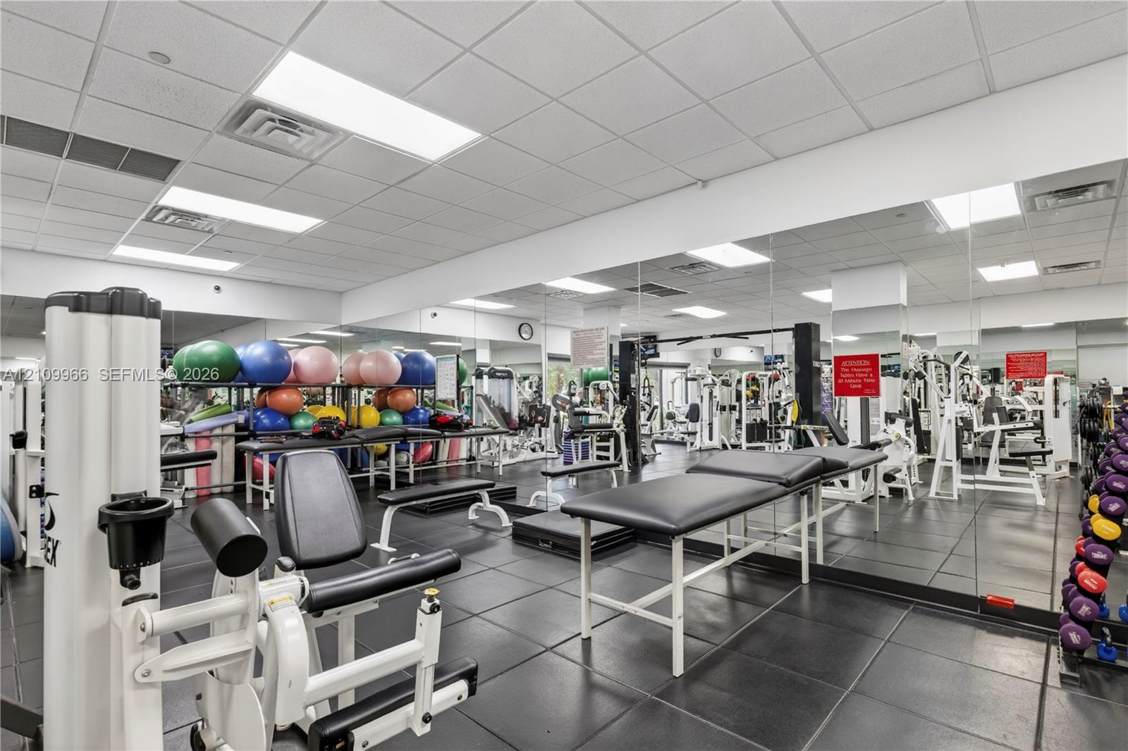 Fitness facility featuring wall-to-wall mirrors, durable rubberized tile flooring, and drop ceiling with recessed lighting