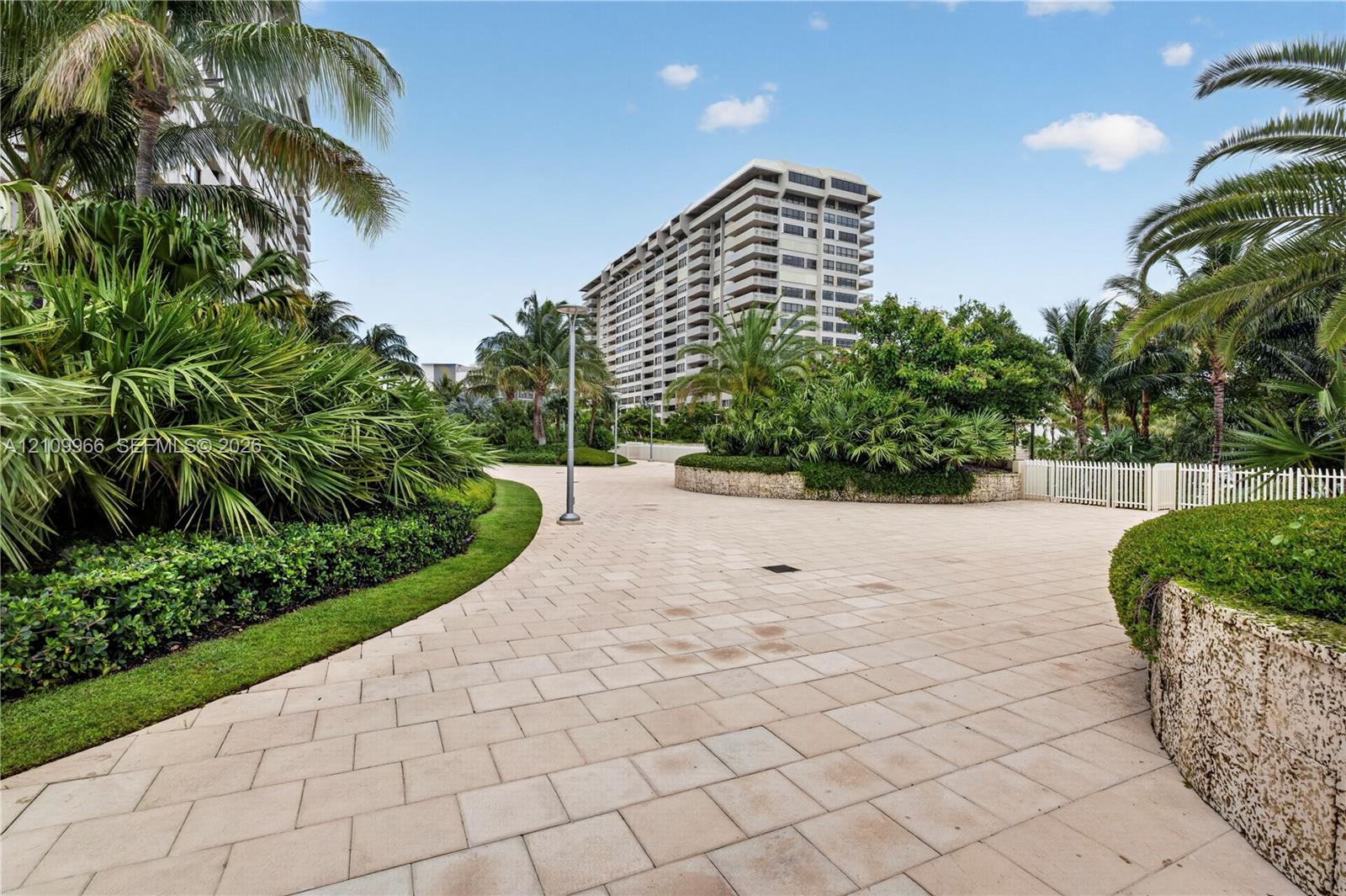 Paved pedestrian walkway featuring stone retaining walls, manicured landscaping, and mature palm trees