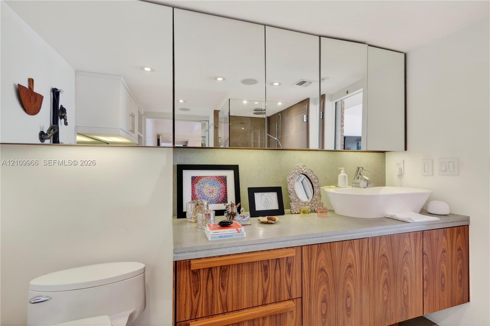 Floating vanity featuring wood-finish cabinetry, a stone-surface countertop, white vessel sink, and an expansive wall-to-wall mirrored medicine cabinet