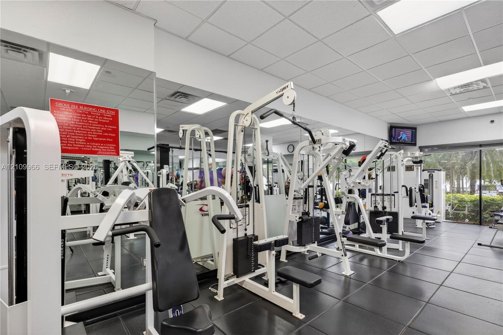 Fitness center featuring modular rubber flooring, full-wall mirrors, recessed drop-ceiling lighting, and floor-to-ceiling windows