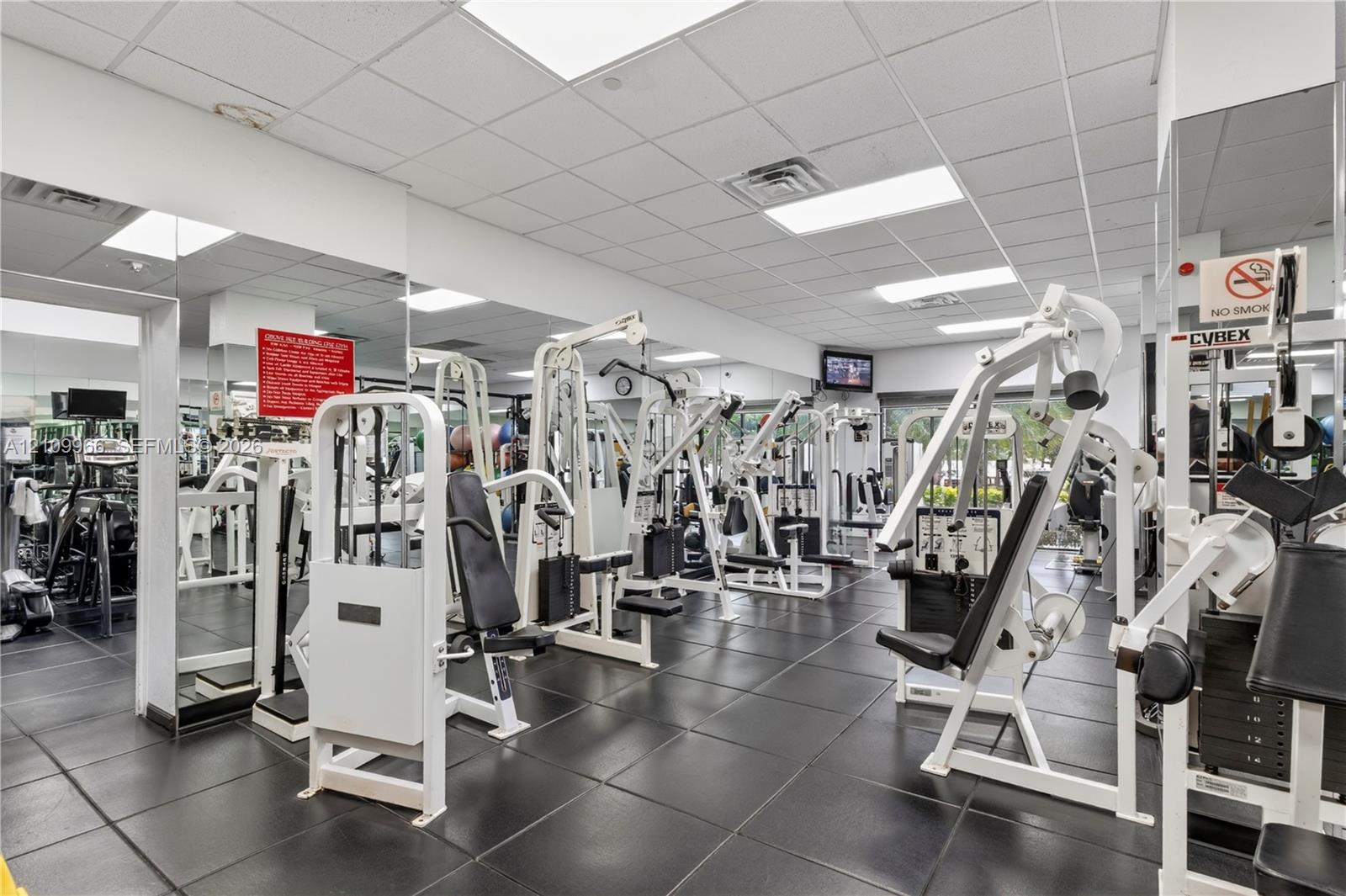 Fitness center featuring rubberized floor tiling, wall-to-wall mirrors, recessed lighting, and a drop ceiling