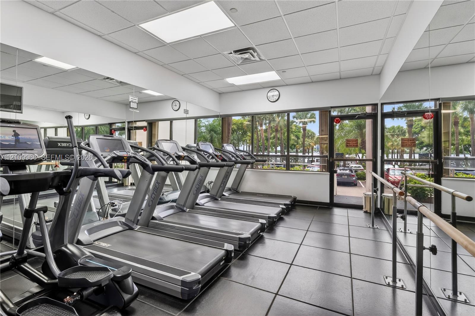 Fitness center featuring large-format tile flooring, floor-to-ceiling mirrored walls, and expansive windows