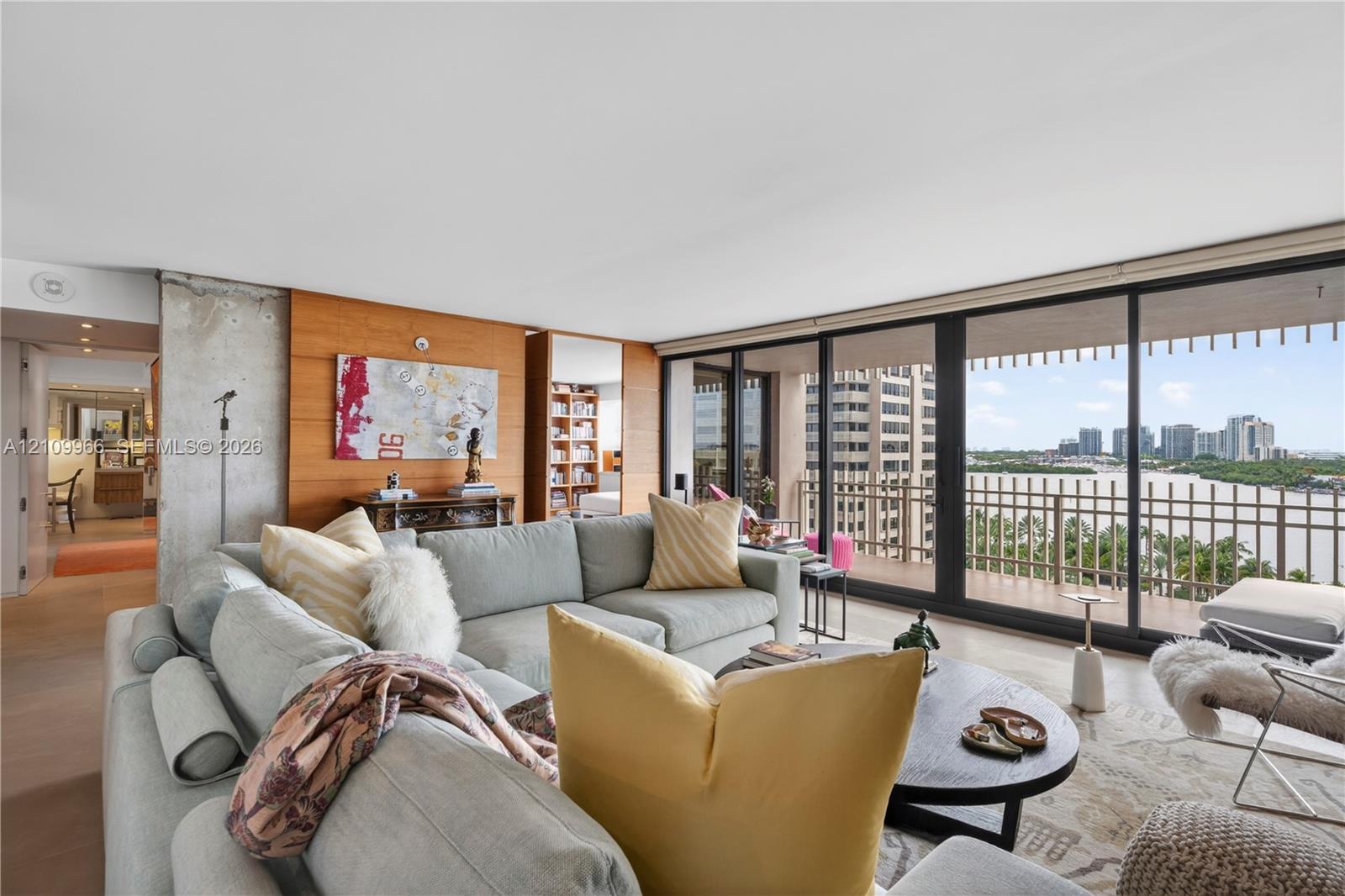 Living area featuring floor-to-ceiling glass sliding doors, wood-paneled walls, exposed concrete structural column, and wood-finish flooring