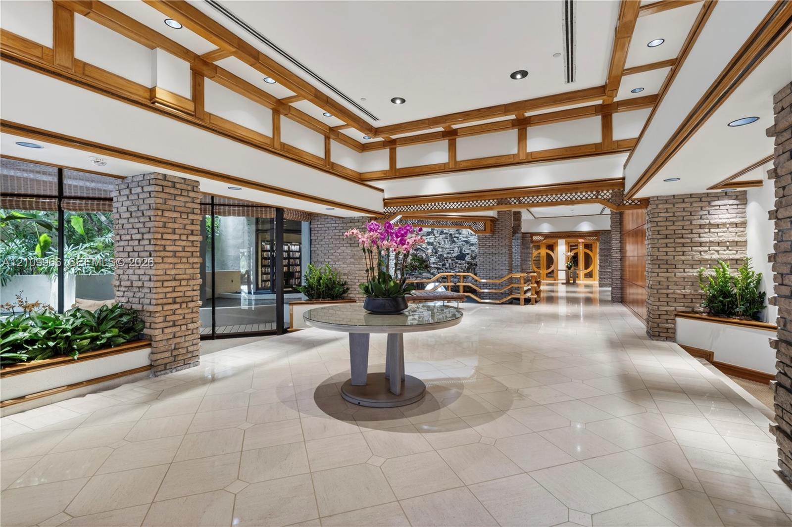 Spacious interior featuring a coffered ceiling with wood trim, decorative brick pillars, tile flooring, and recessed lighting