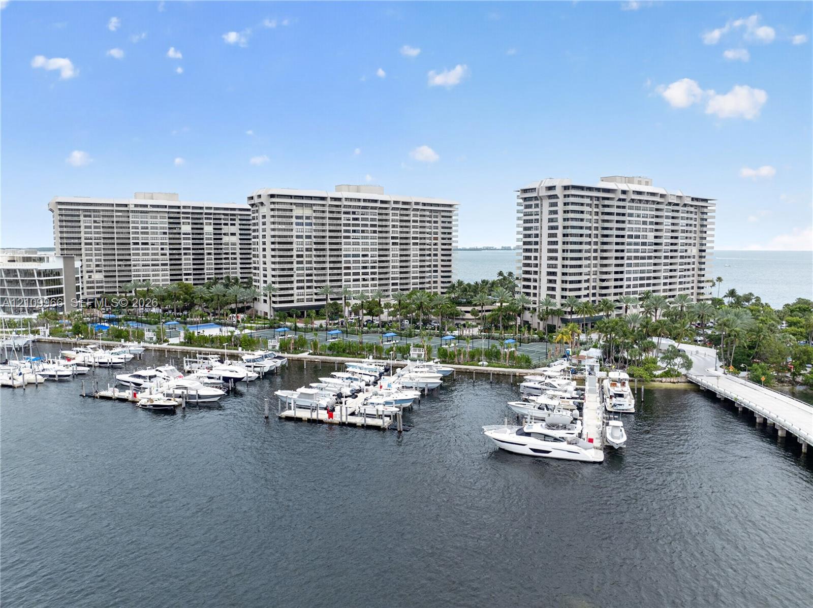 High-rise residential complex featuring a deep-water marina, private boat slips, extensive waterfront hardscaping, and lush tropical landscaping