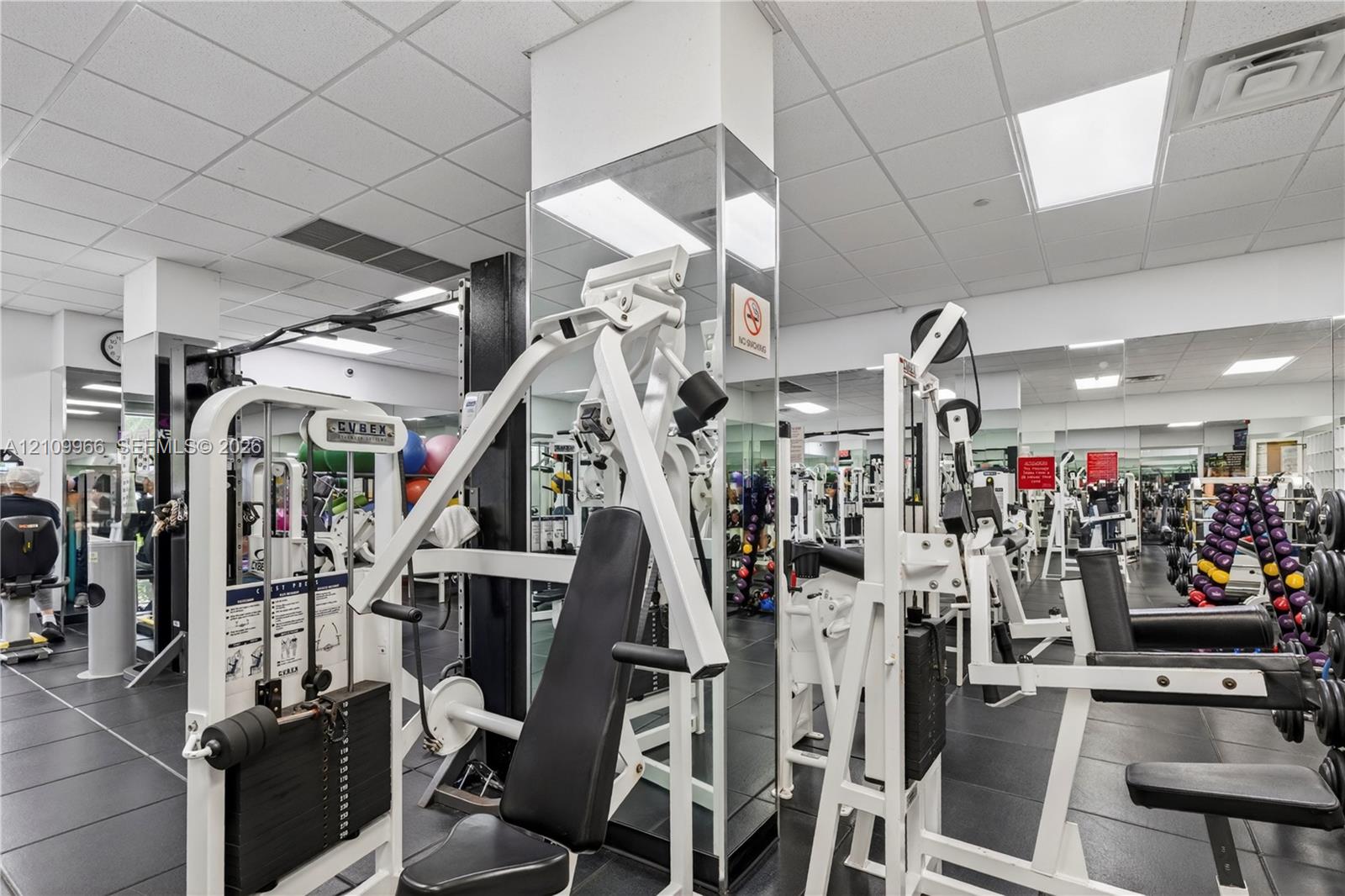 Fitness center featuring grid ceiling tiles, wall-to-wall mirrors, and durable rubber flooring
