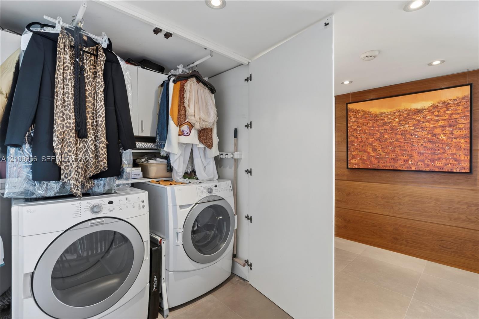 Laundry area featuring white front-load washer and dryer, built-in white cabinetry, wood-panel wall accents, and tile flooring