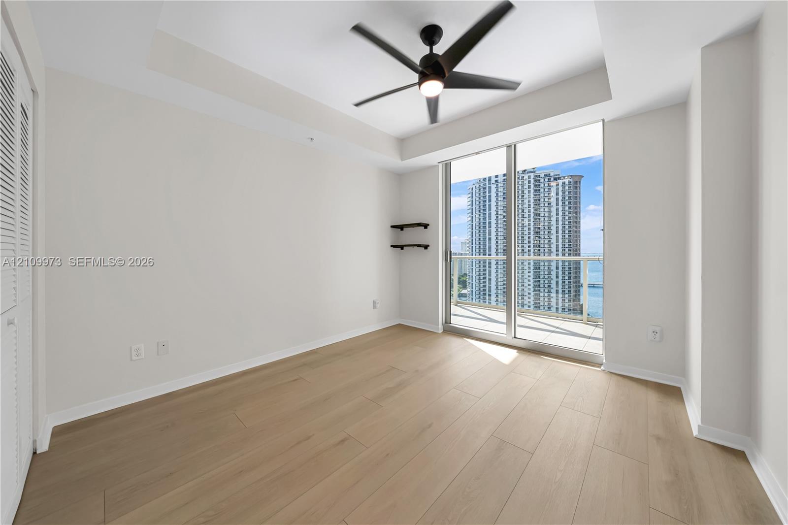 Room featuring wood-finish flooring, a coffered ceiling with a built-in fan, and floor-to-ceiling glass sliding doors opening to a balcony