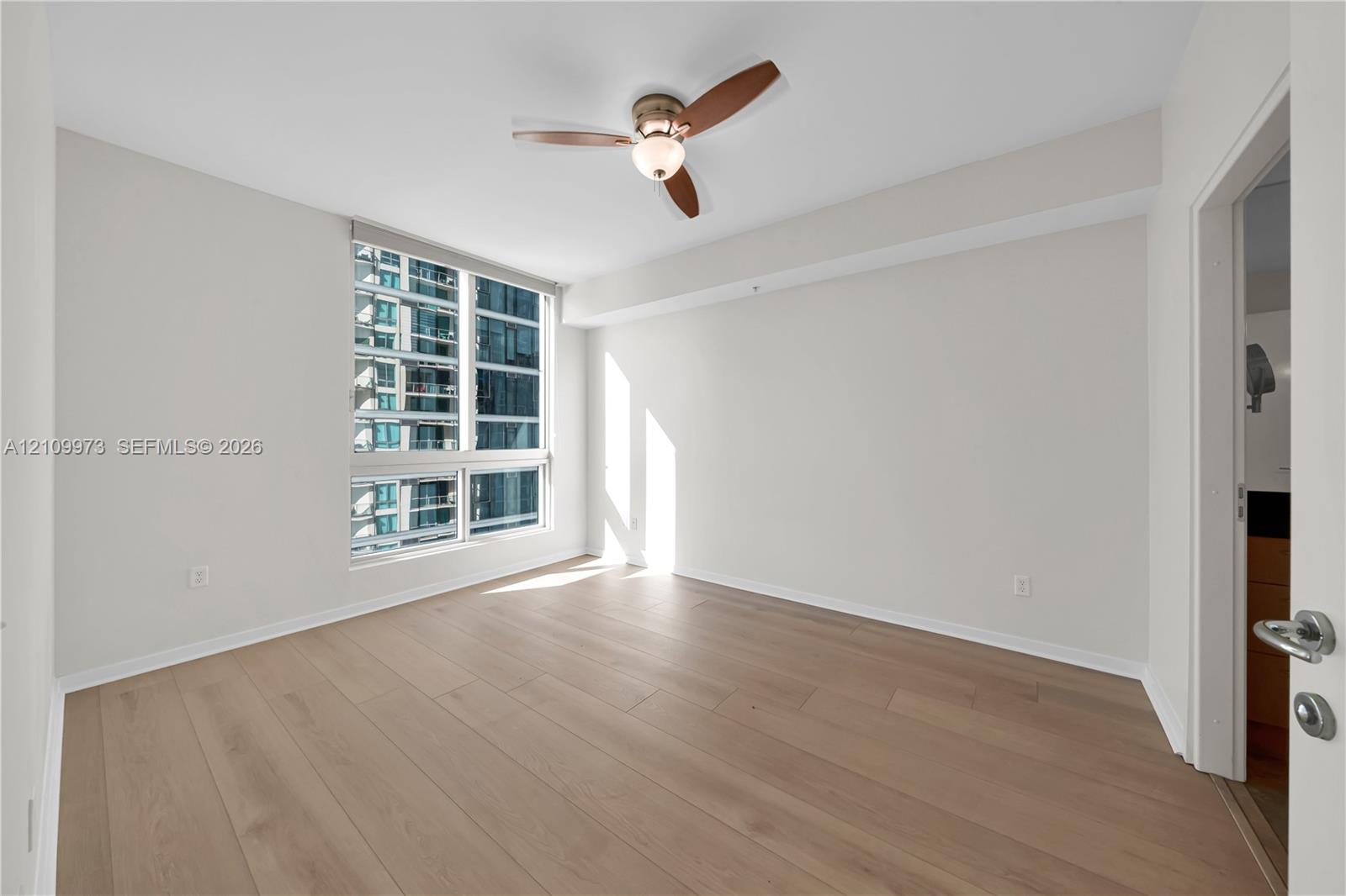 Neutral-toned interior featuring wide-plank wood-finish flooring, floor-to-ceiling windows, and a three-blade ceiling fan with an integrated light fixture