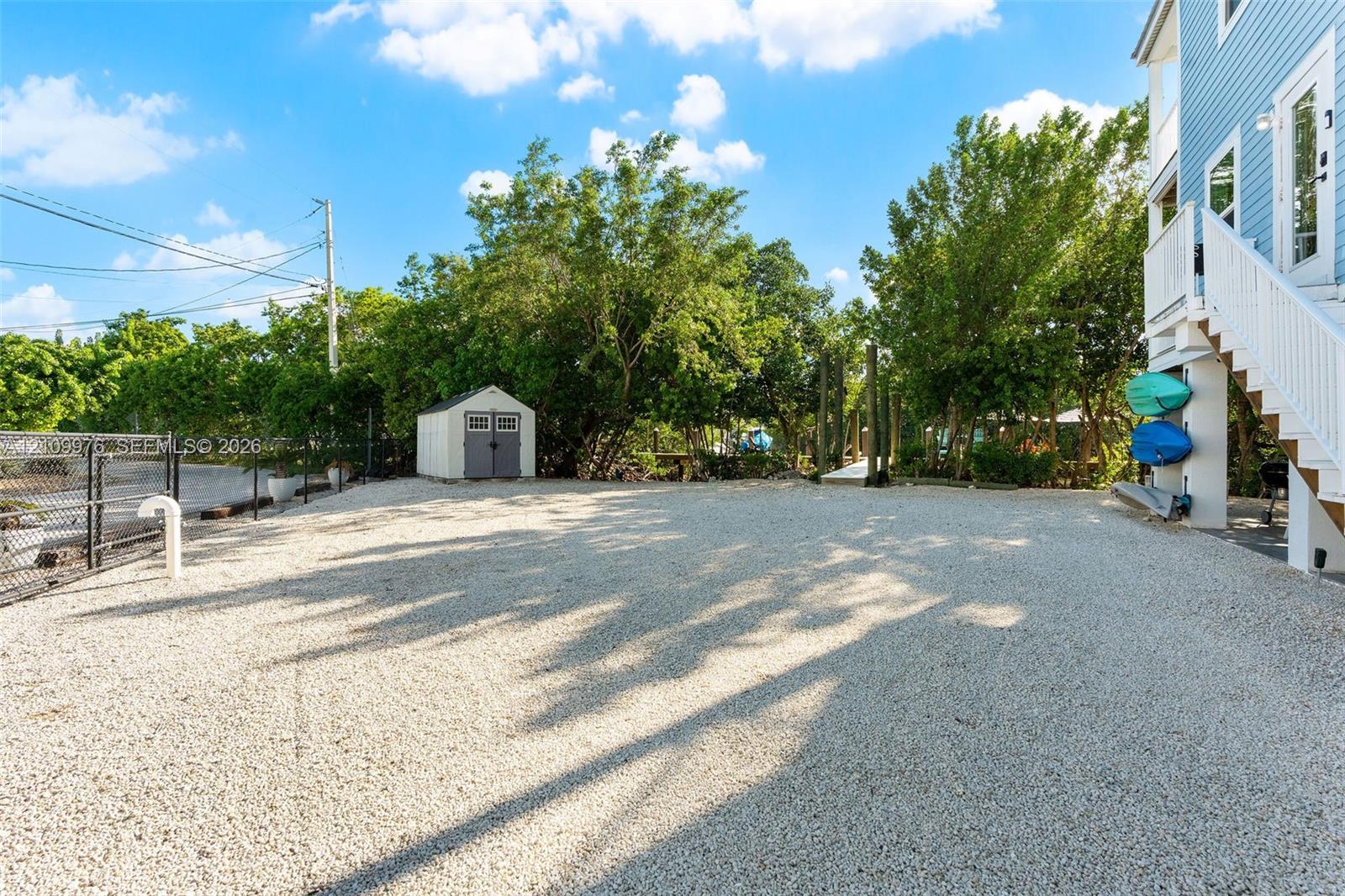 Gravel-surfaced exterior lot featuring a detached storage shed, perimeter chain-link fencing, and elevated home foundation
