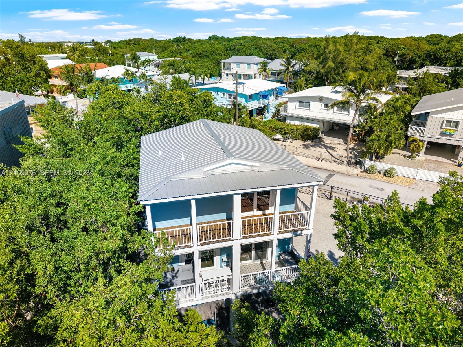 Two-story property featuring a metal roof, stacked exterior balconies with white railings, and a gravel driveway