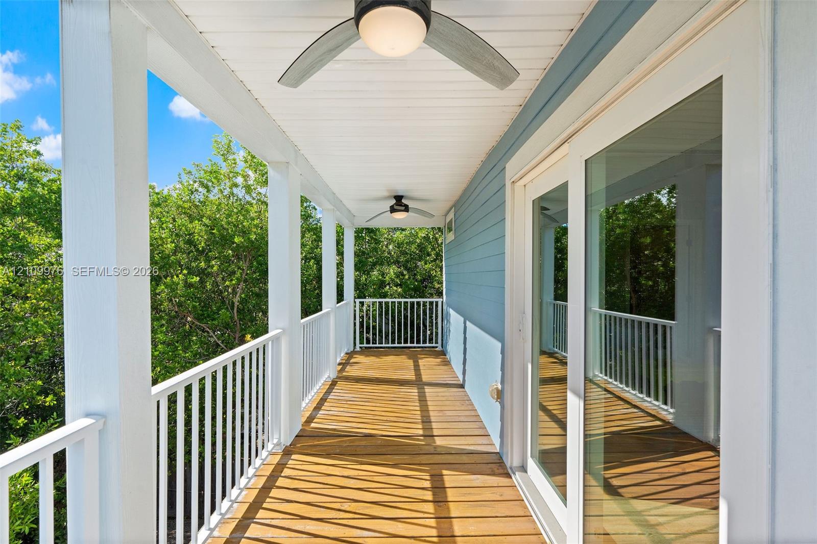 Covered balcony featuring wood-plank flooring, white metal railing, dual ceiling fans with integrated lighting, and horizontal lap siding