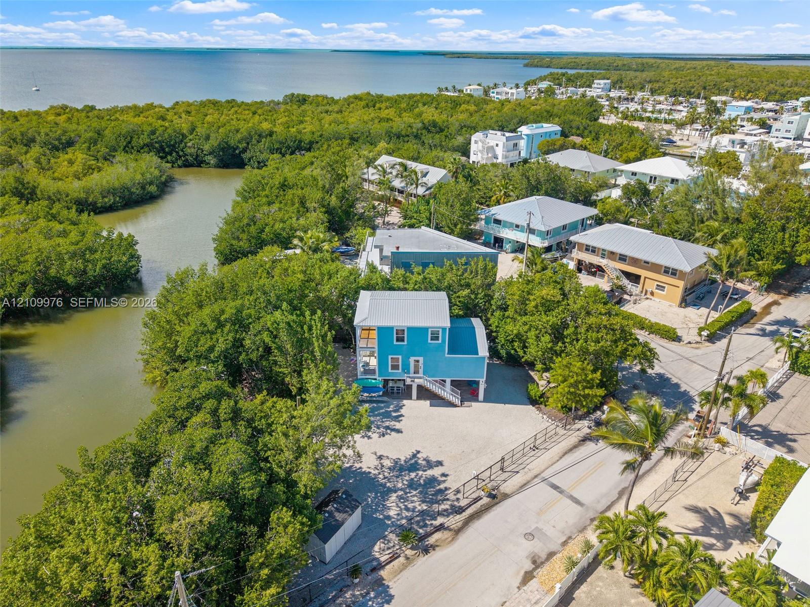 Elevated residence featuring a metal roof, light-toned gravel lot, and waterfront positioning along a natural canal