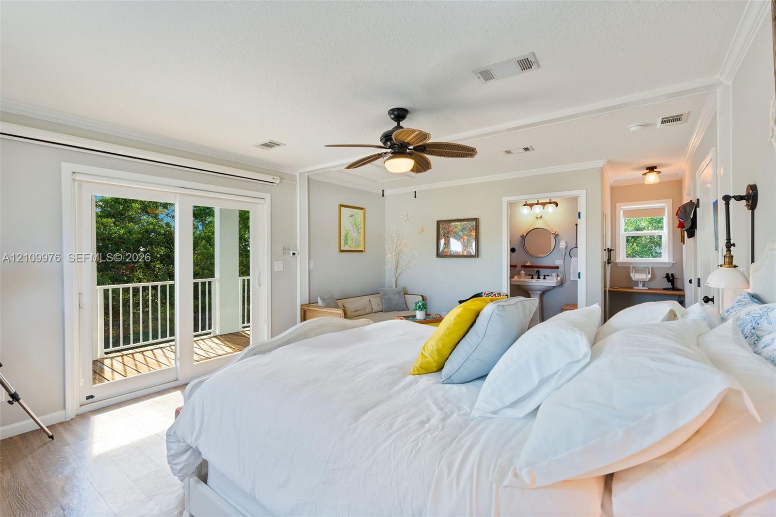 Room featuring wood-finish flooring, a ceiling fan with integrated lighting, glass sliding doors opening to an exterior balcony, crown molding, and an attached washroom with a pedestal sink and vanity mirror