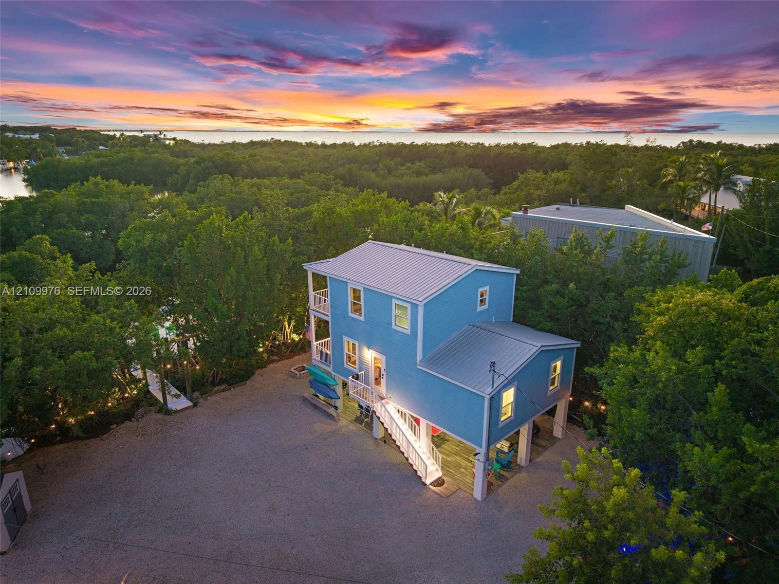 Elevated multi-level residence featuring a metal roof, wraparound balconies, exterior staircase, and a sprawling gravel grounds area Elevated multi-level residence featuring a metal roof, wraparound balconies, exterior staircase, and a sprawling gravel grounds area