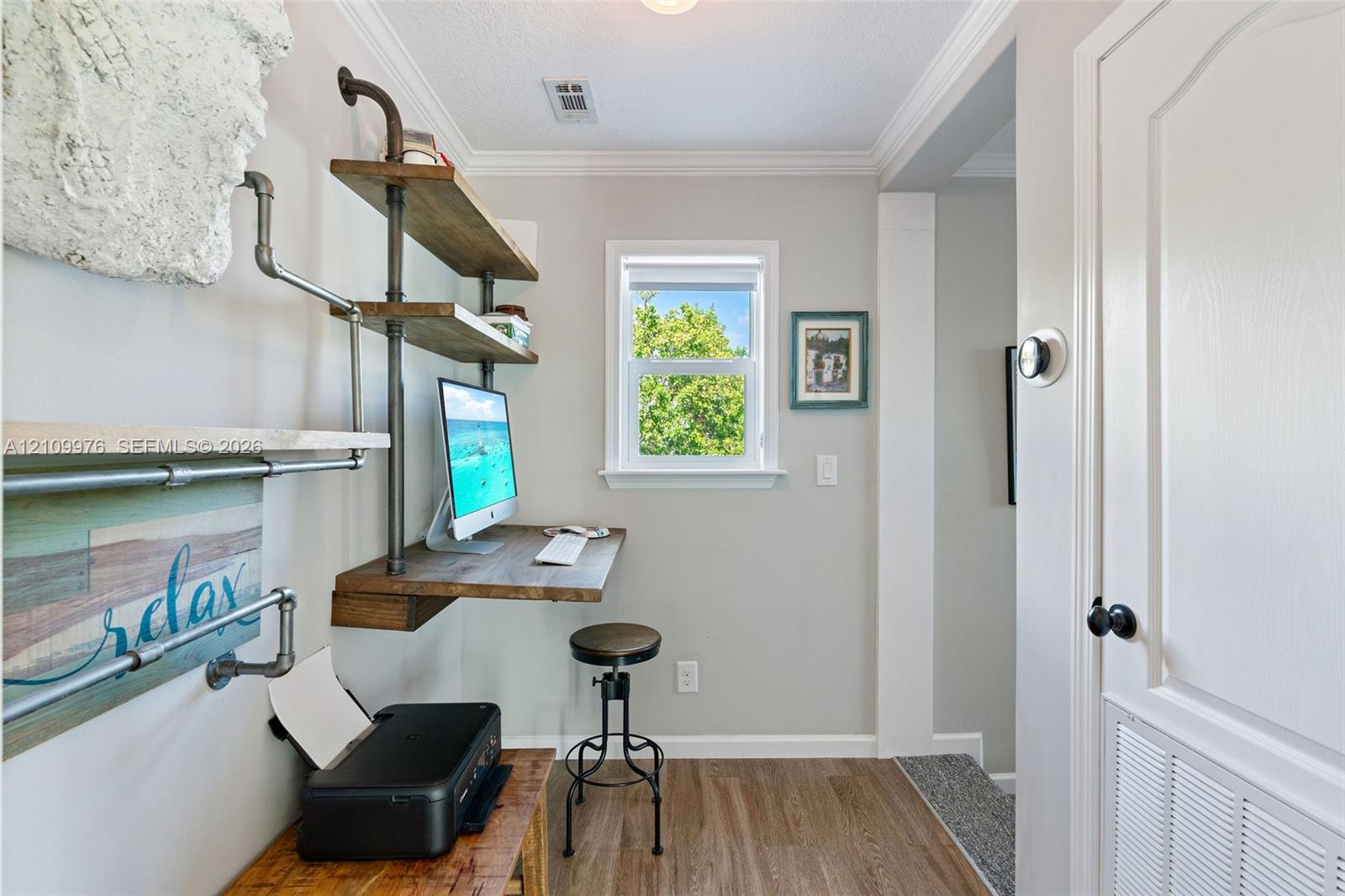 Built-in industrial-style shelving with wood-finish surfaces, wall-mounted desk, crown molding, and wood-finish flooring