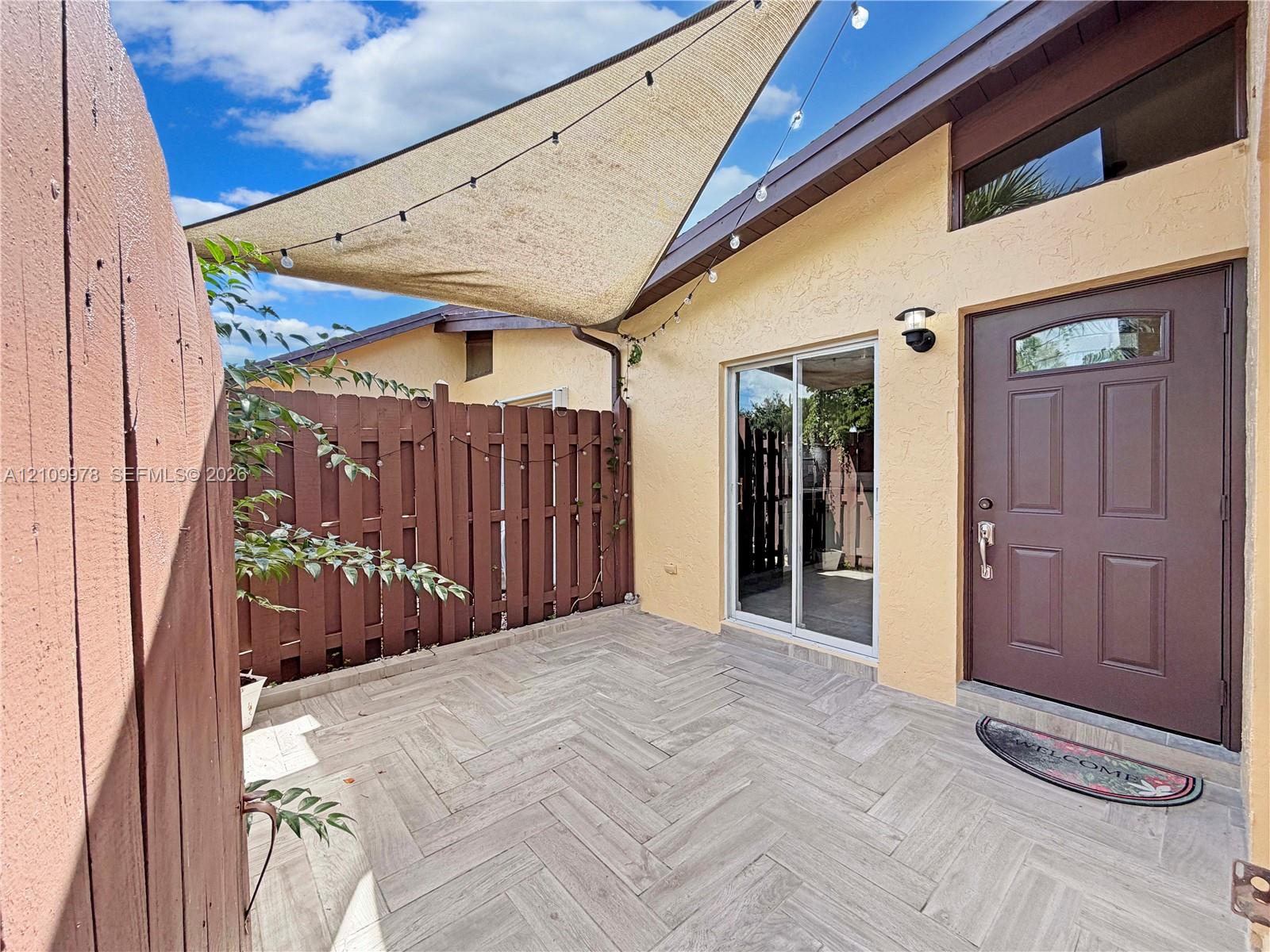Private courtyard featuring herringbone-patterned tile flooring, a solid wood privacy fence, sliding glass door, and a six-panel exterior door with a transom window Private courtyard featuring herringbone-patterned tile flooring, a solid wood privacy fence, sliding glass door, and a six-panel exterior door with a transom window