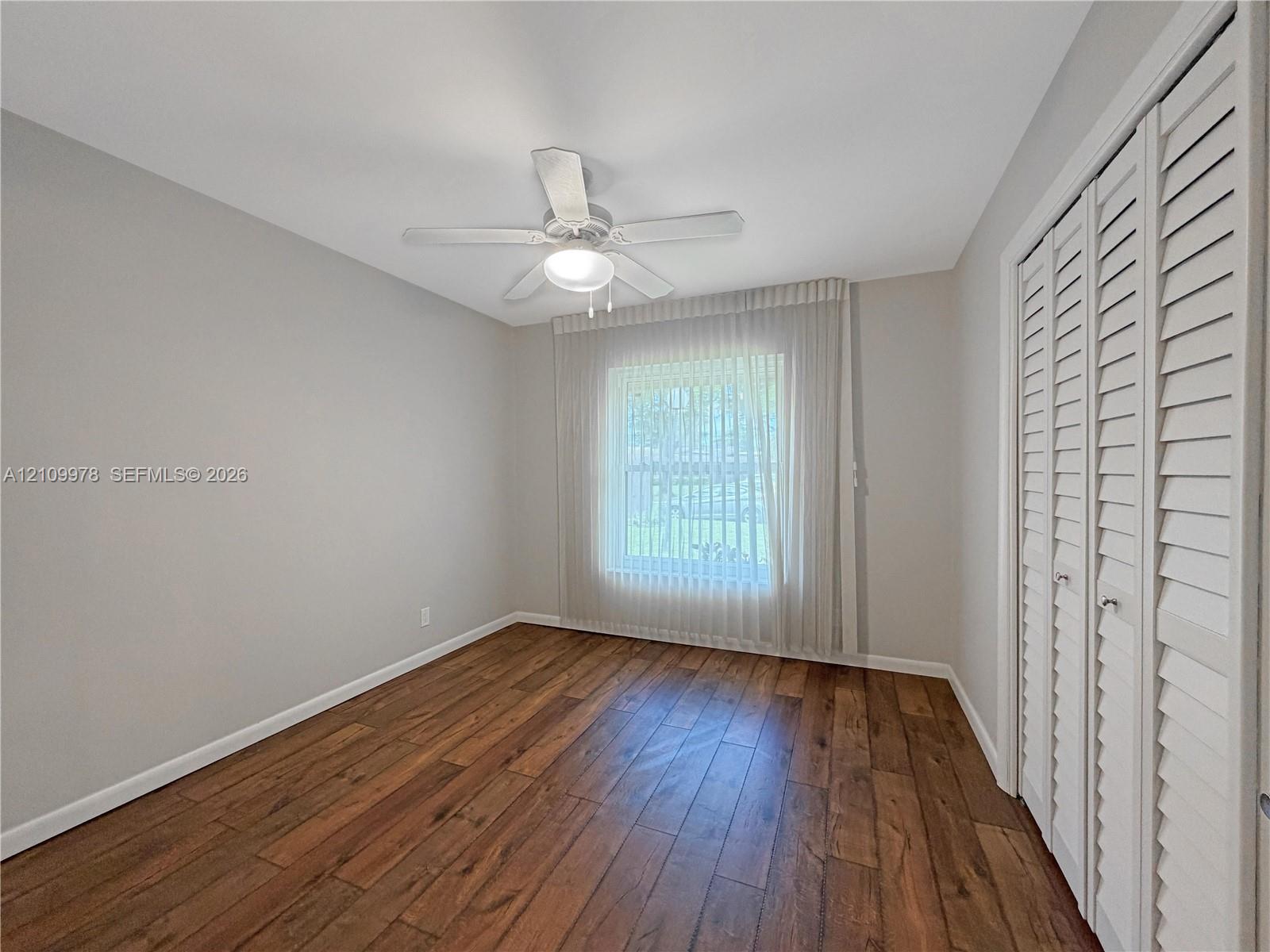 Room featuring wood-finish flooring, white louvered closet doors, and a ceiling fan with integrated lighting