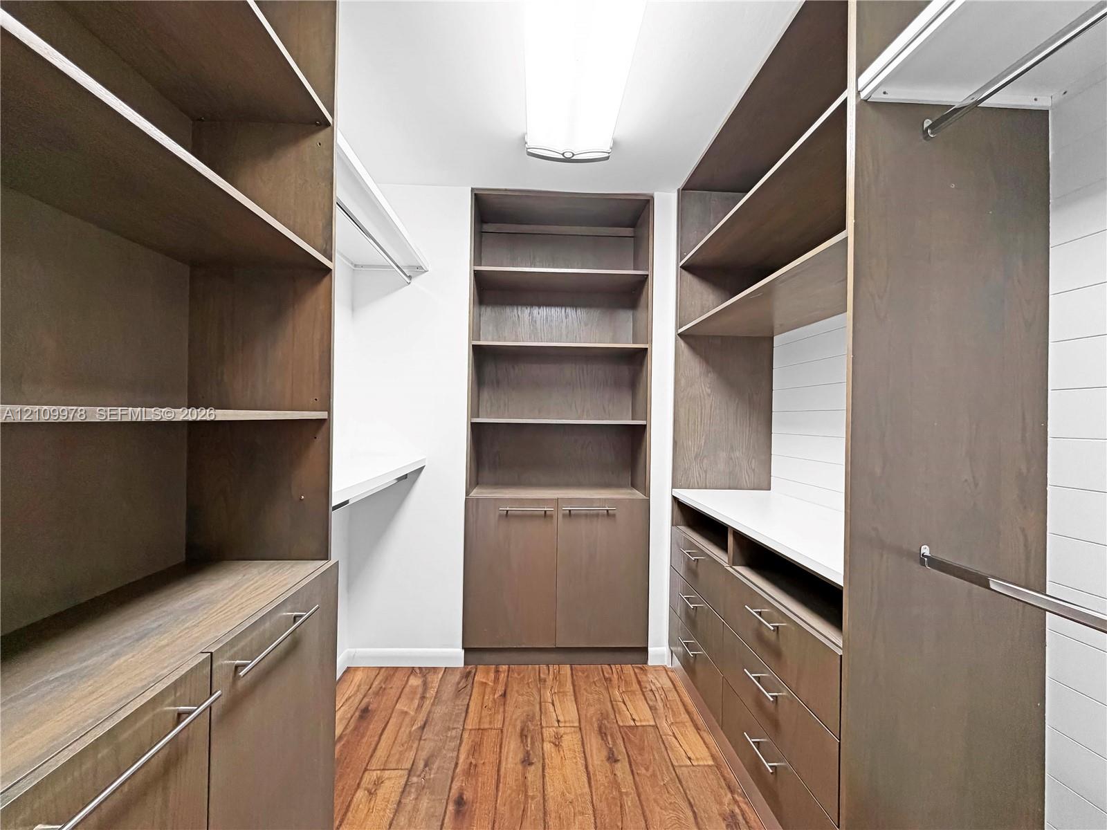 Custom walk-in closet featuring extensive wood-finish cabinetry, built-in drawer units, adjustable shelving, integrated hanging rods, and wood-finish flooring