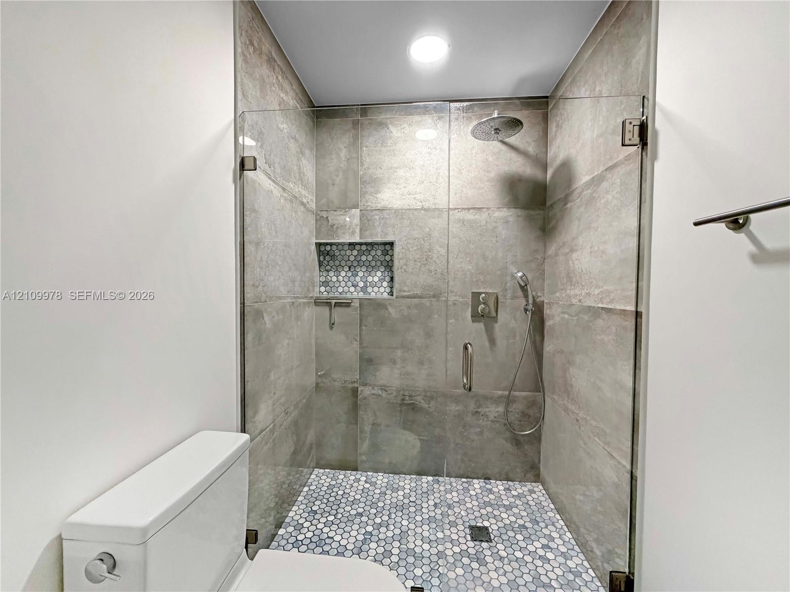 Walk-in shower featuring large-format wall tile, a mosaic-tiled floor and inset niche, a frameless glass enclosure, and dual-function rainfall and handheld shower fixtures