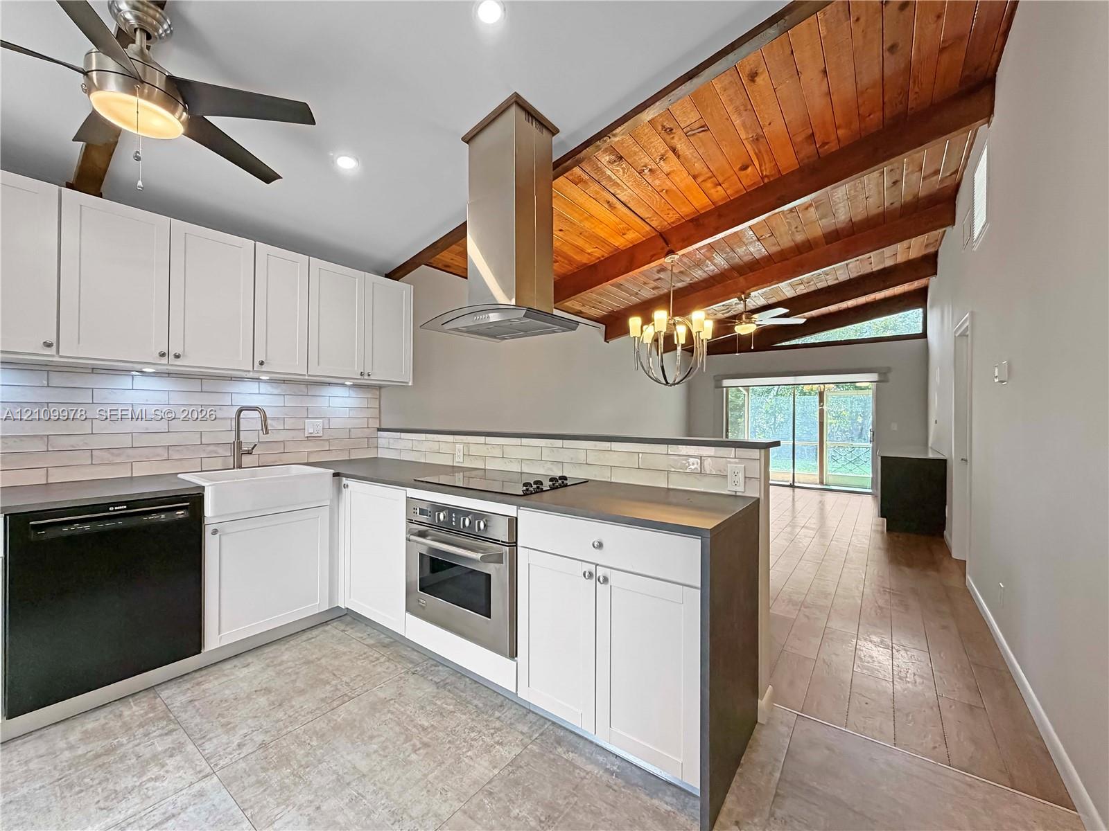 Kitchen featuring white shaker cabinetry, a farmhouse-style sink, stainless steel appliances, a tile backsplash, and wood-paneled vaulted ceilings Kitchen featuring white shaker cabinetry, a farmhouse-style sink, stainless steel appliances, a tile backsplash, and wood-paneled vaulted ceilings