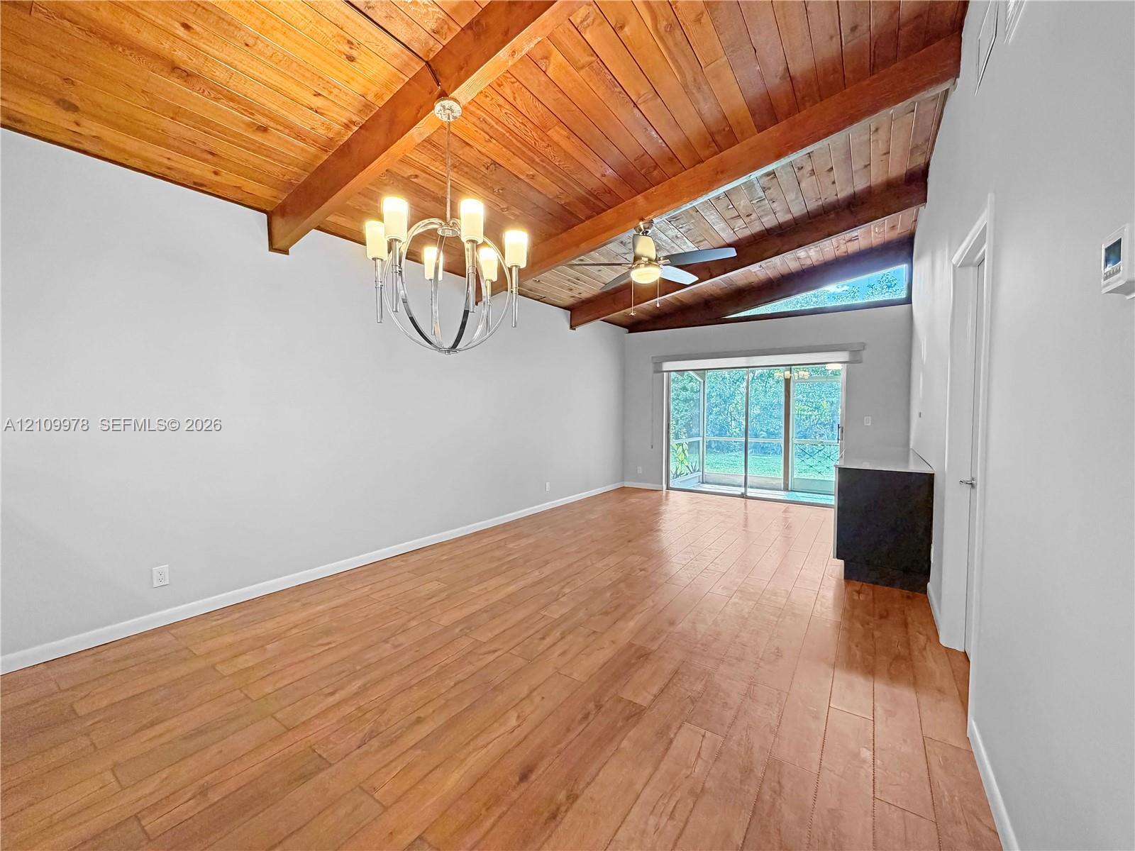 Vaulted ceiling with exposed wood beams, wood-finish flooring, metal chandelier, ceiling fan, and sliding glass doors Vaulted ceiling with exposed wood beams, wood-finish flooring, metal chandelier, ceiling fan, and sliding glass doors