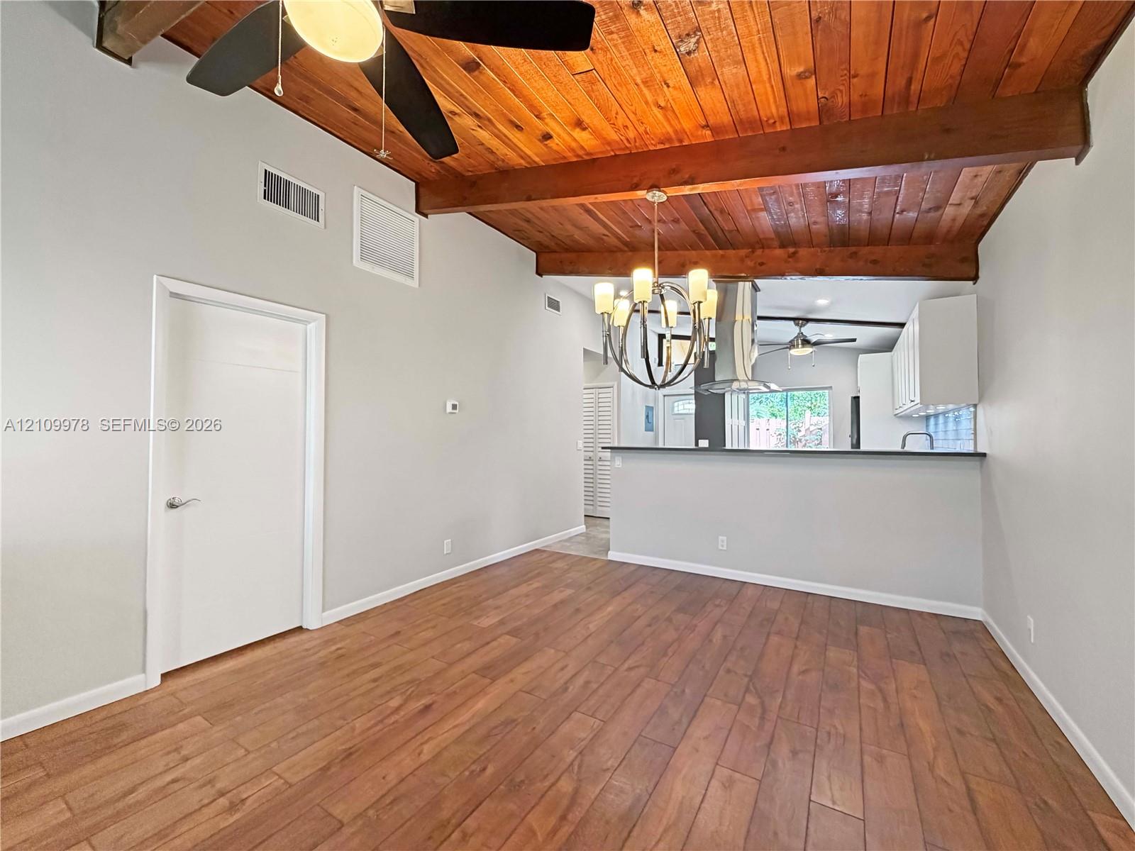Vaulted ceilings featuring exposed wood beams, wood-finish flooring, a multi-arm chandelier, and an open-concept kitchen partition Vaulted ceilings featuring exposed wood beams, wood-finish flooring, a multi-arm chandelier, and an open-concept kitchen partition